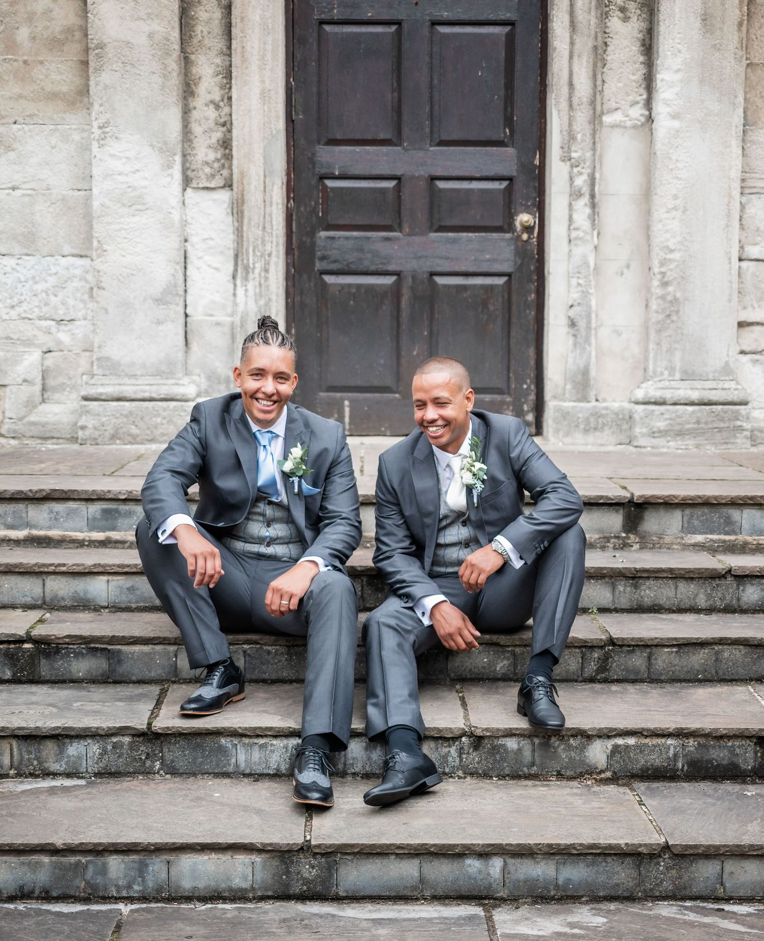 Two people in matching suits share a relaxed moment sitting on stone steps.