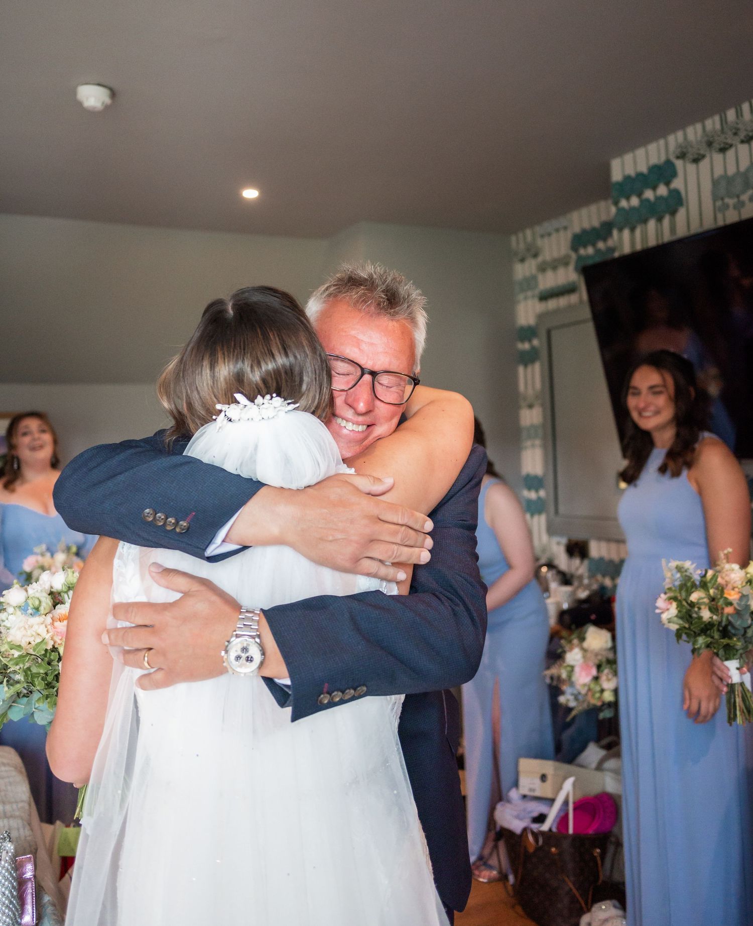 A tender wedding embrace shared during a celebration with bridesmaids in light blue dresses looking on.
