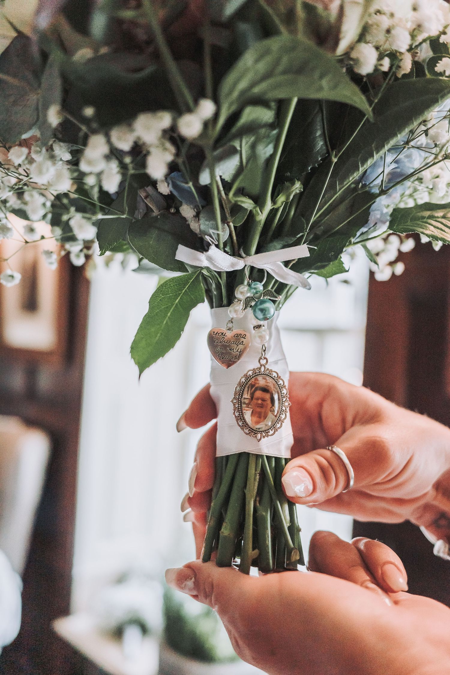 Wedding bouquet detail showing a sentimental photo charm attached to the flower stems.