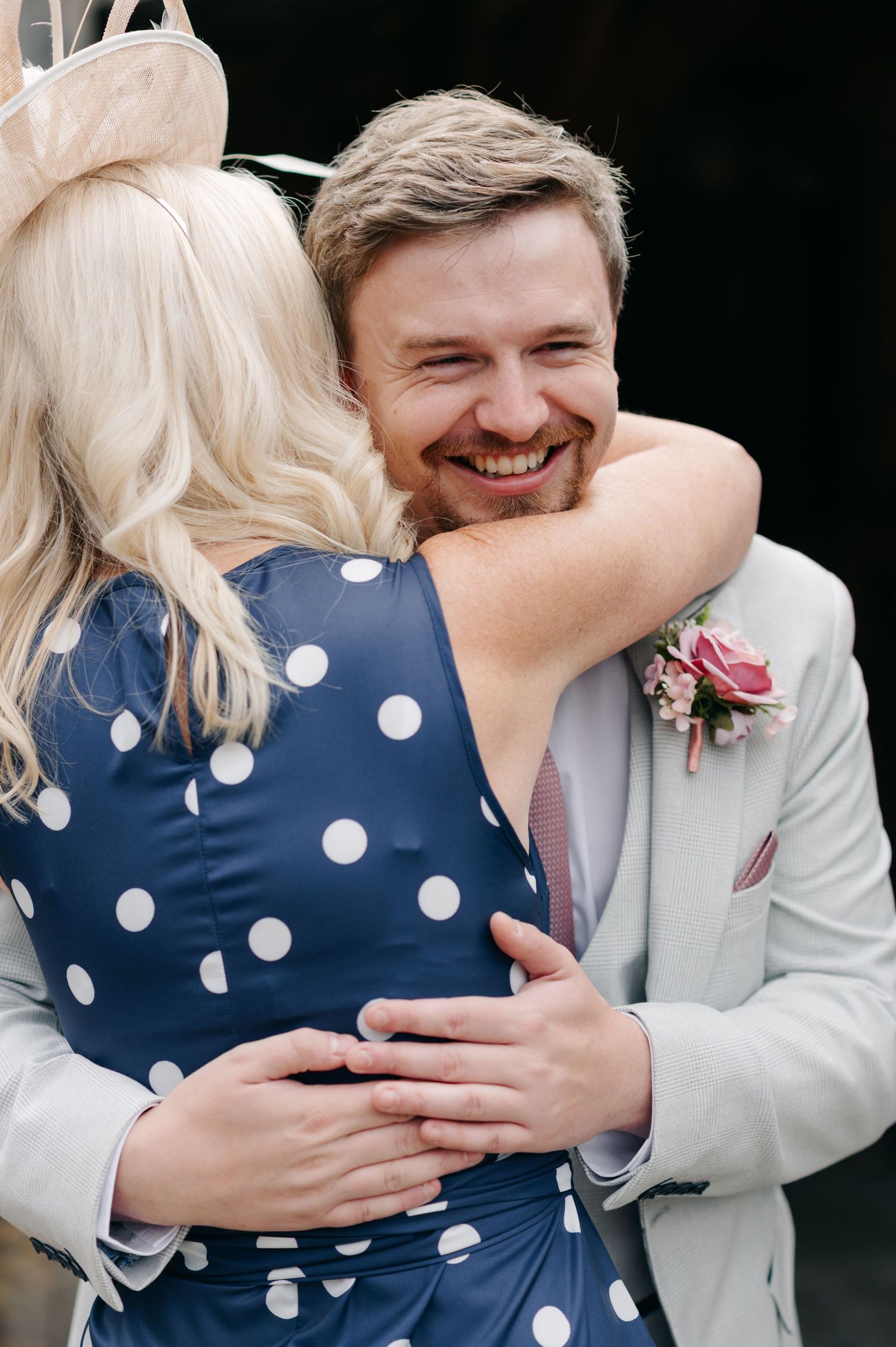 A couple embraces and shares a joyful moment in their wedding attire, with the bride in a polka dot dress.
