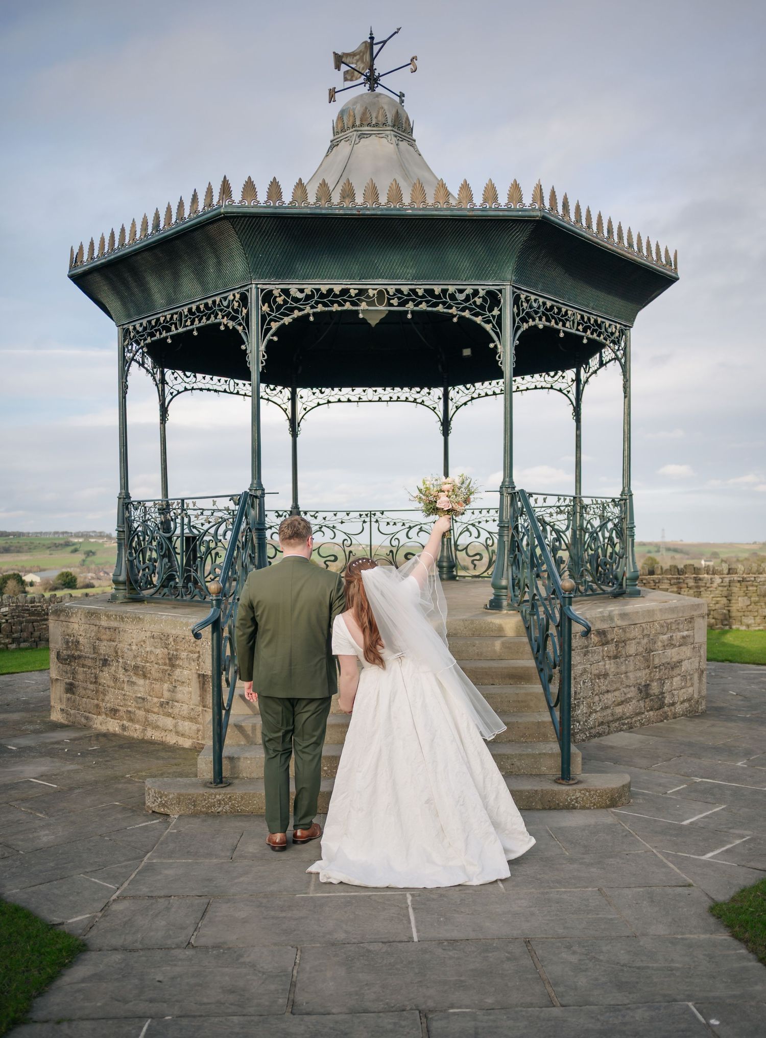 Wedding couple poses at a Victorian-style gazebo overlooking scenic countryside views.