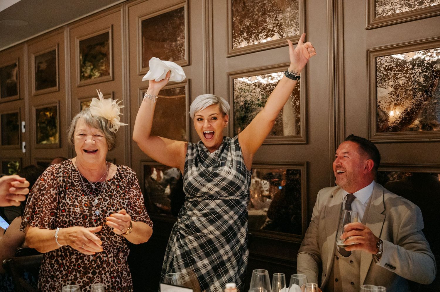 Wedding guests celebrating and cheering during reception dinner in an elegant dining room.