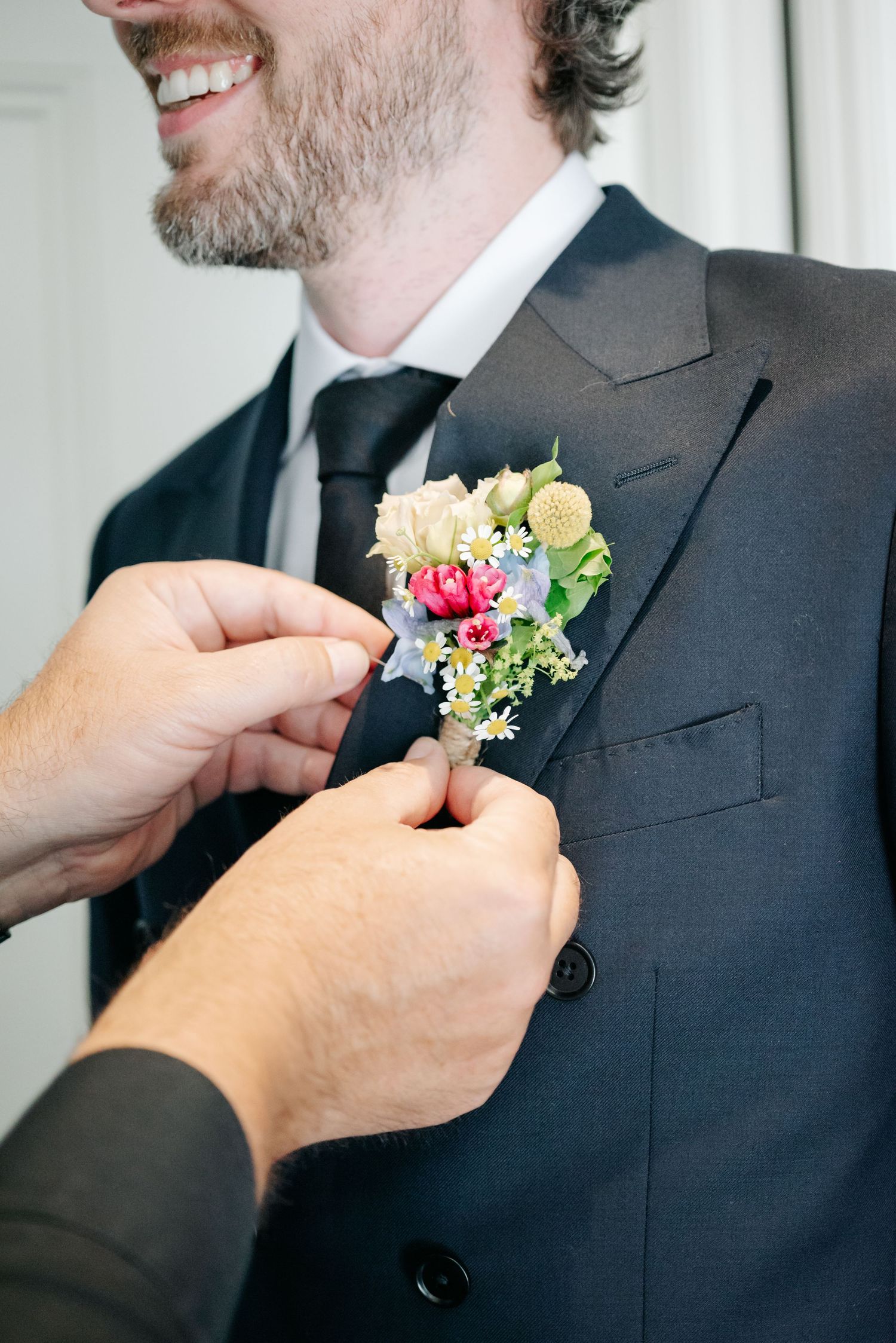 Close-up sequence of hands pinning a floral boutonniere onto a dark suit jacket.