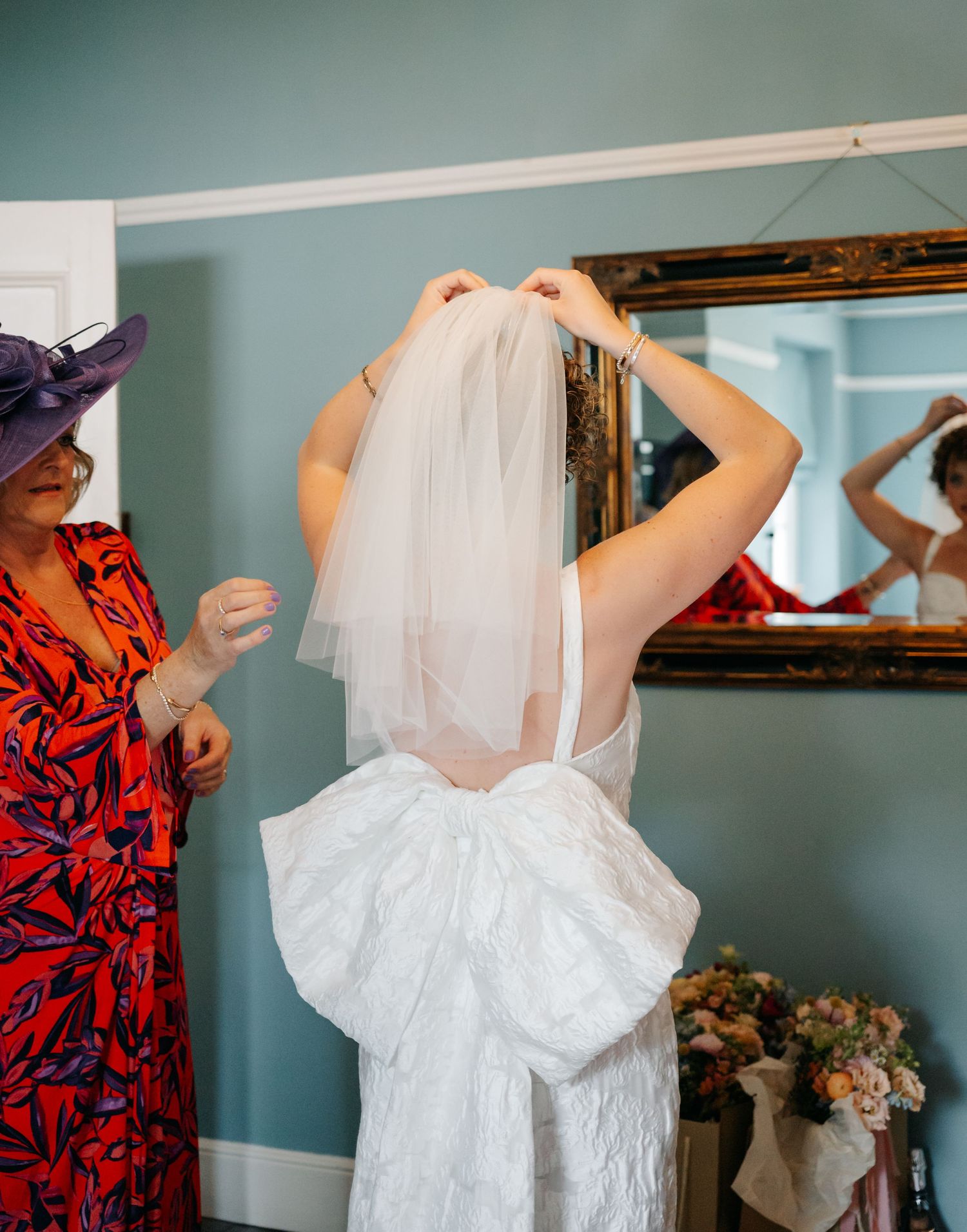 Wedding dress being prepared and fluffed in a blue-walled dressing room.