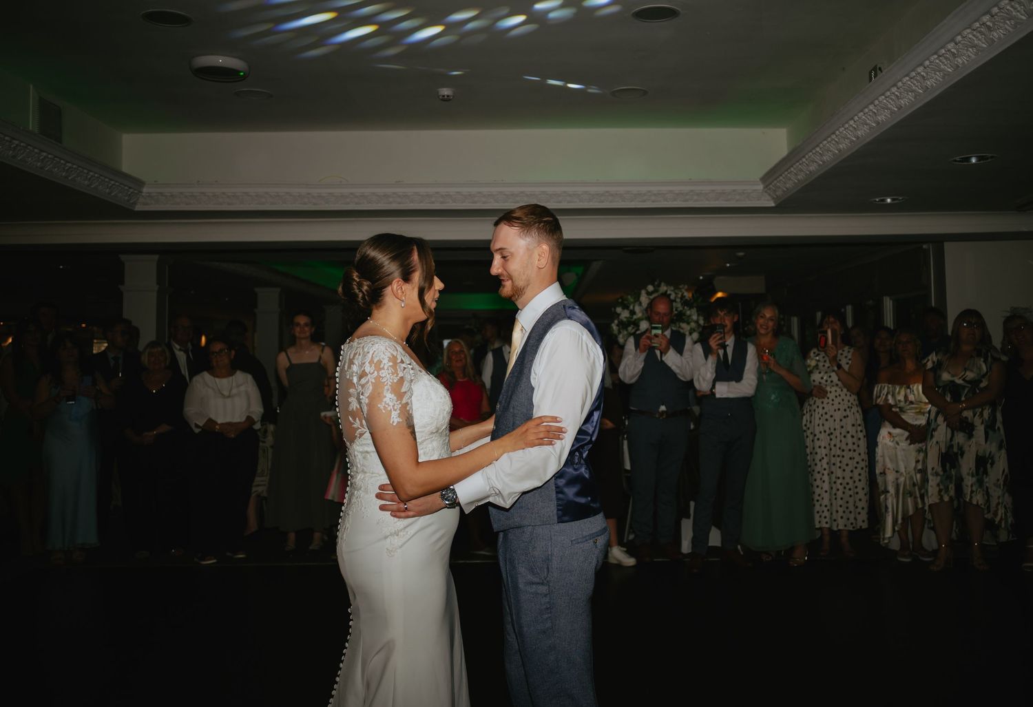 A couple shares their first dance surrounded by guests at their wedding reception.