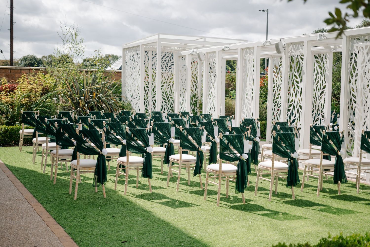 White pergola structures and green chairs set up for an outdoor wedding ceremony.