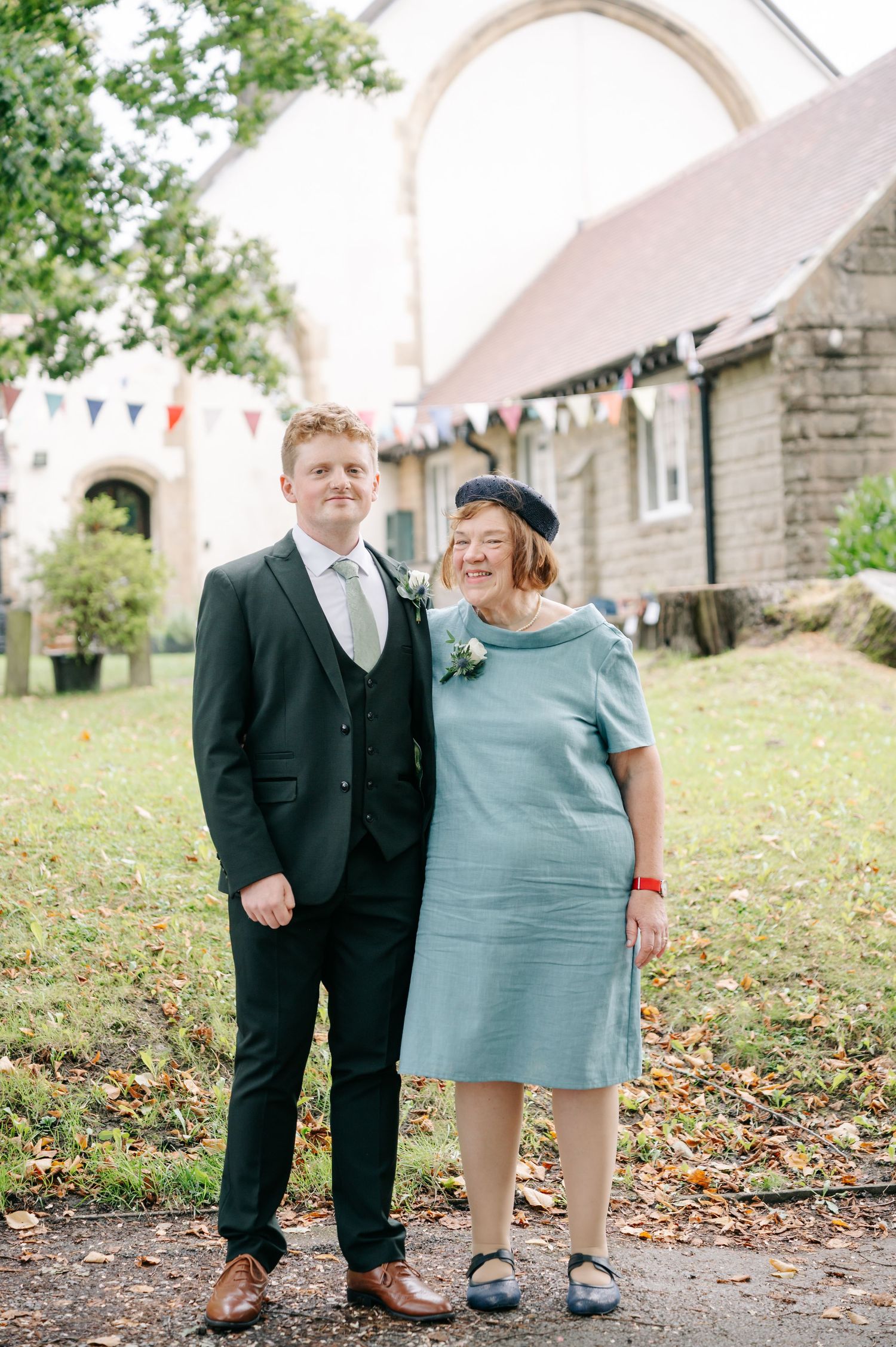Couple in formal attire poses together on a leaf-covered path during an autumn wedding.