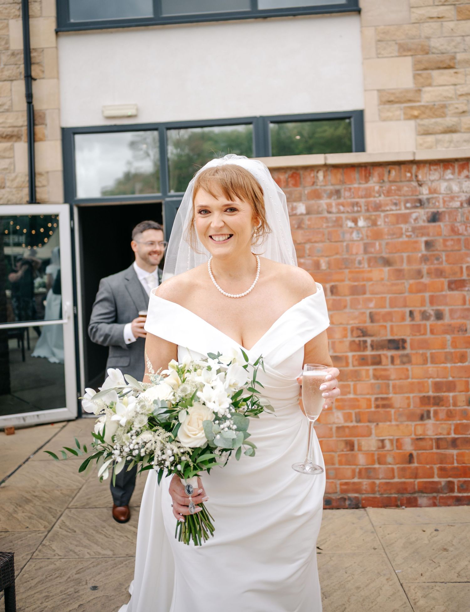 A joyful moment captured outside a brick building with white floral bouquet and off-shoulder dress.