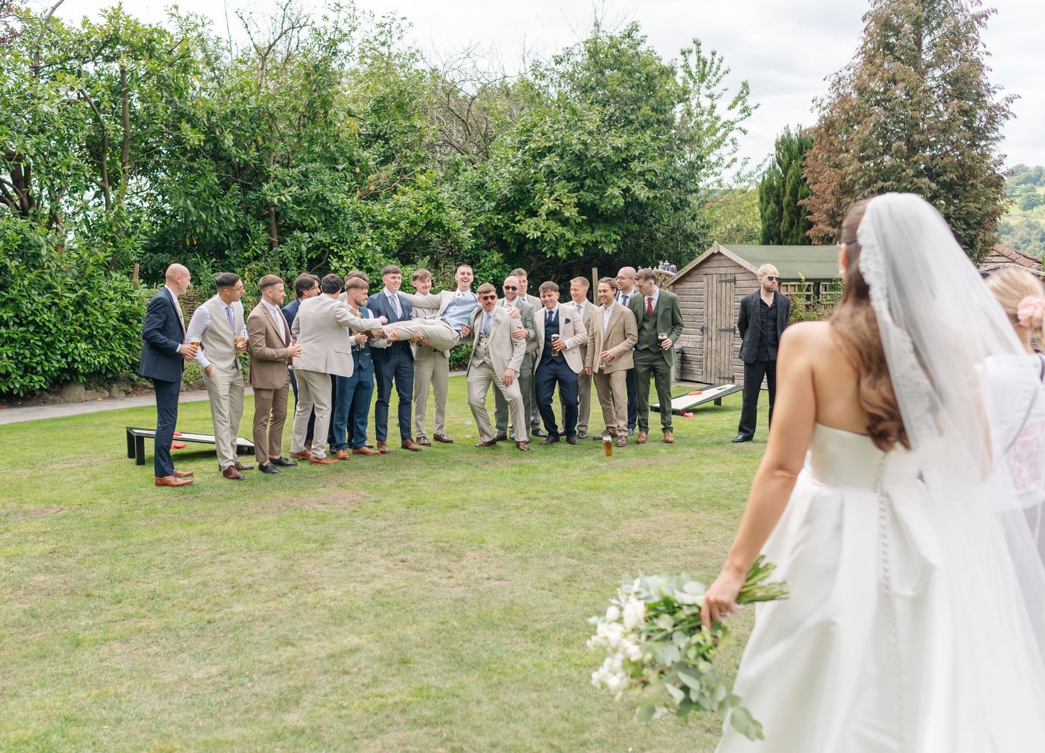 Wedding party standing in a line outdoors with green grass and trees in the background.