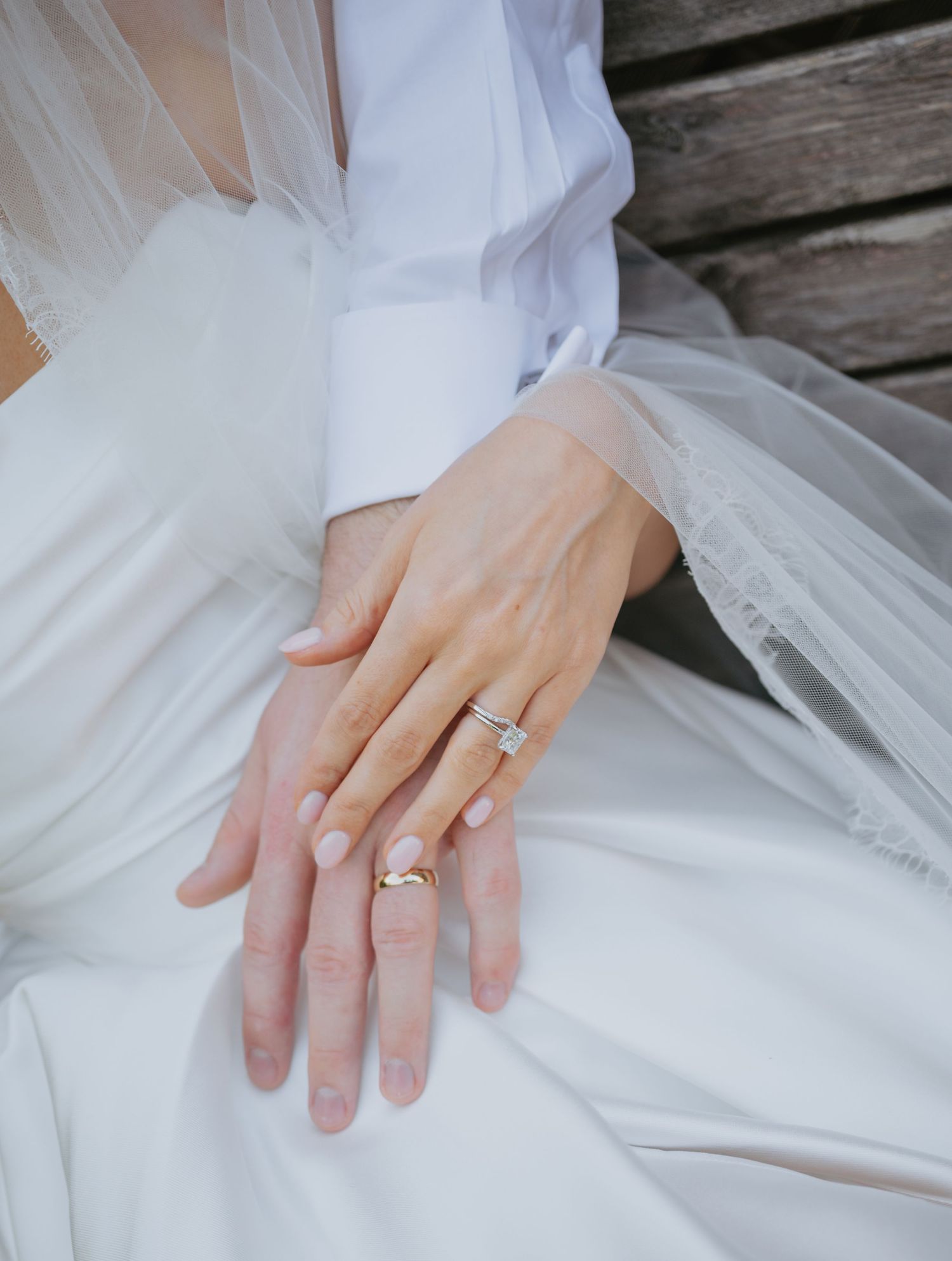 Close-up of hands showing wedding ring details on white dress fabric.