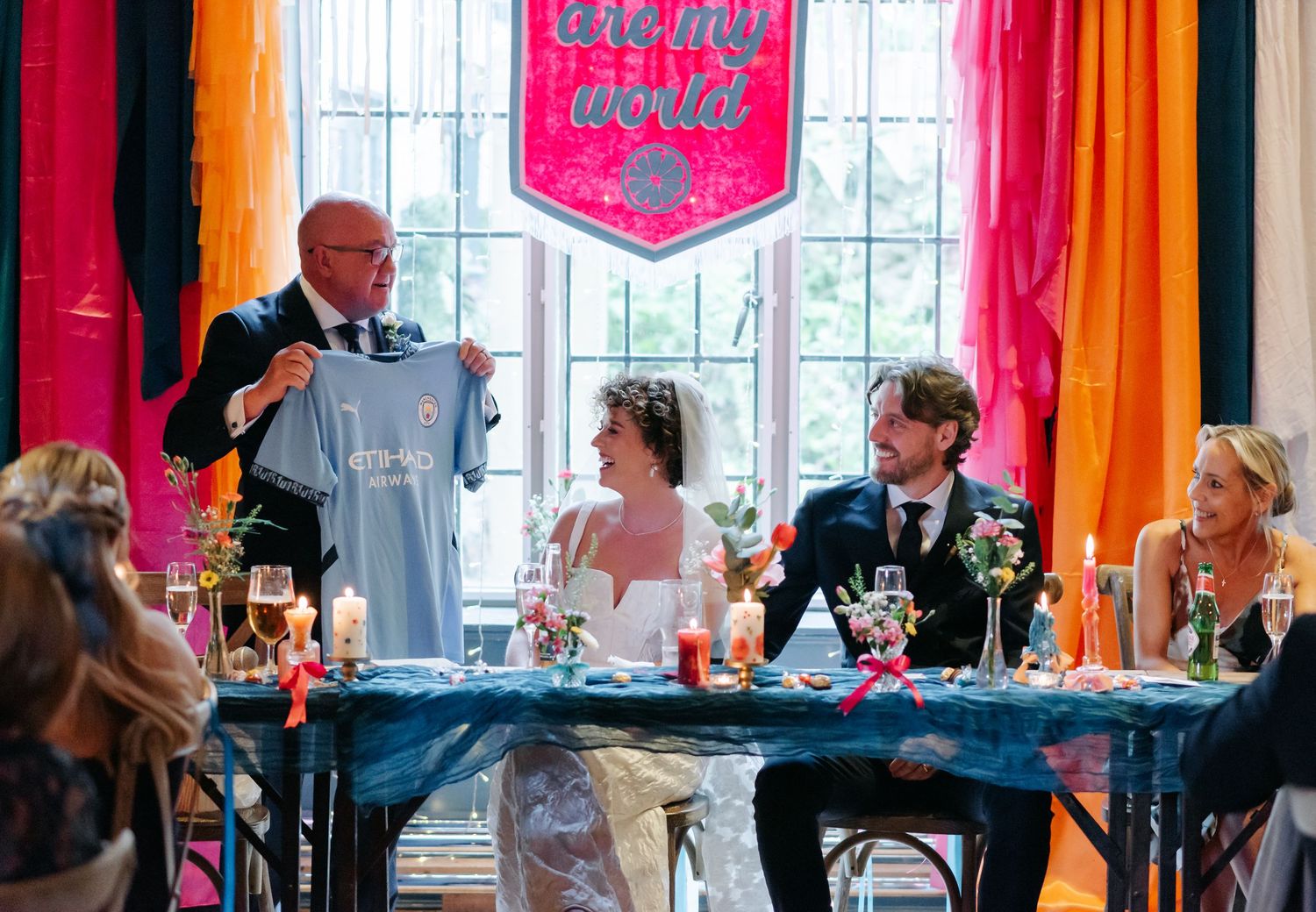 Wedding reception hall decorated with vibrant orange and pink drapes and window light.