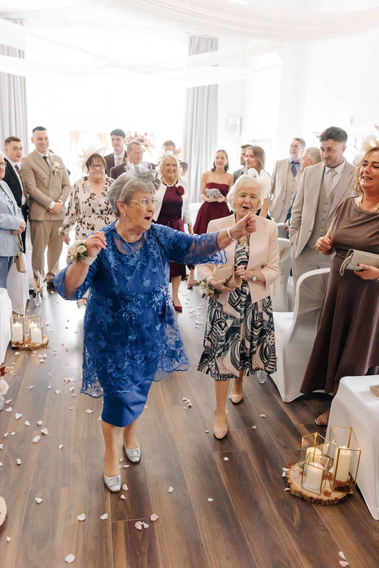 Wedding guests dancing and celebrating on a wooden dance floor with scattered flower petals.