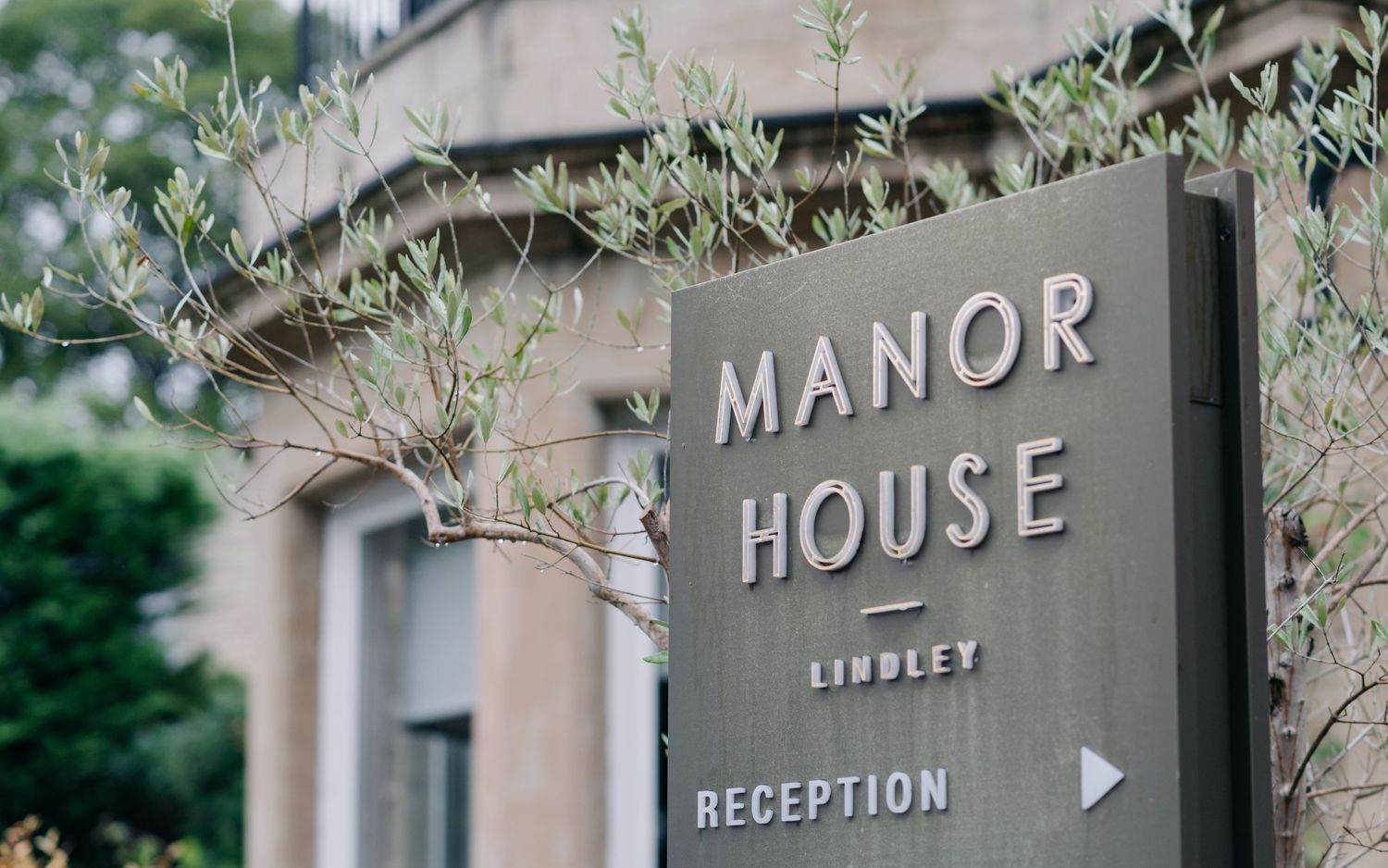 A series of elegant manor house directional signs mounted on stone walls with lush green foliage in the background.