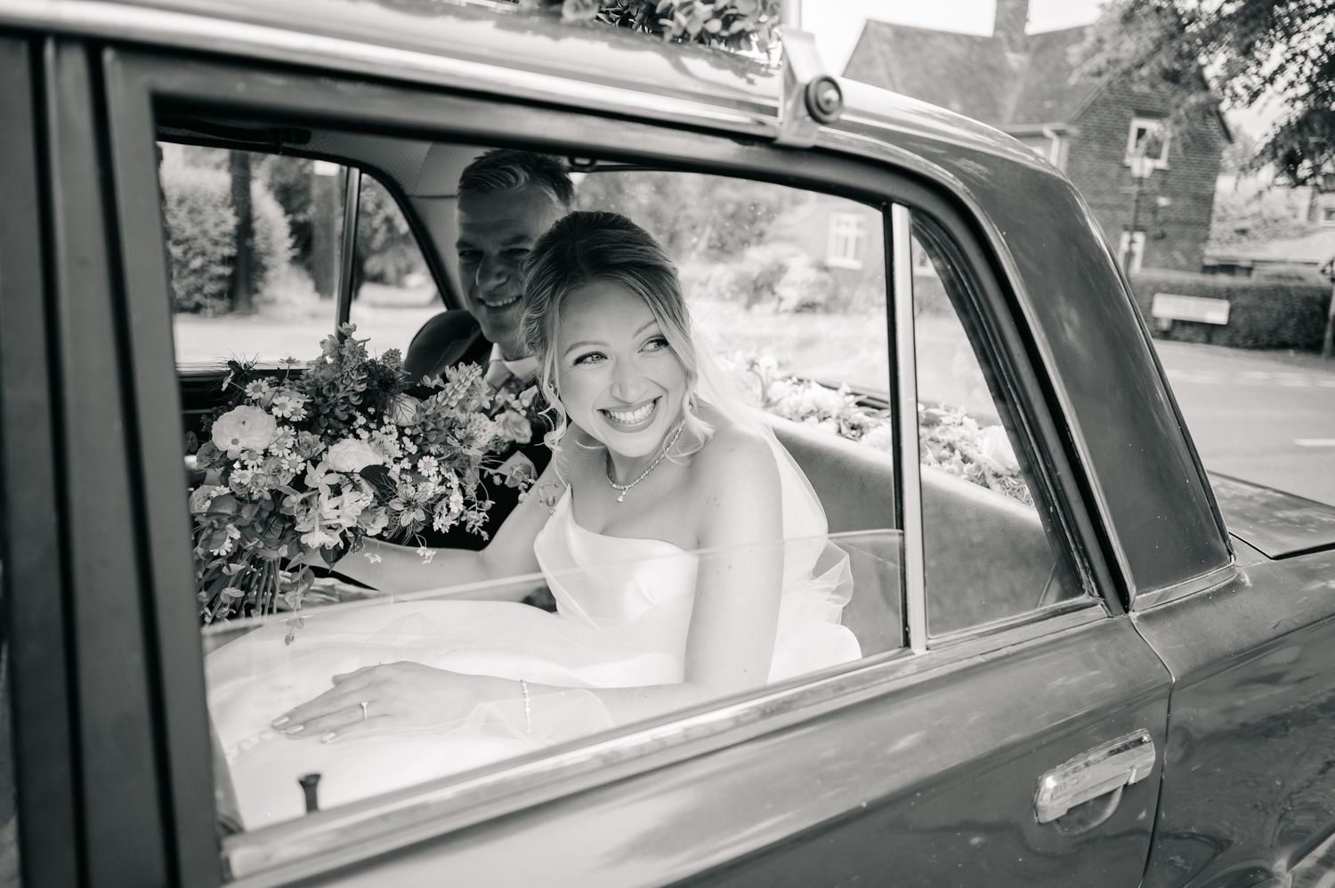 A joyful moment captured in black and white of a bride sitting in a vintage car.