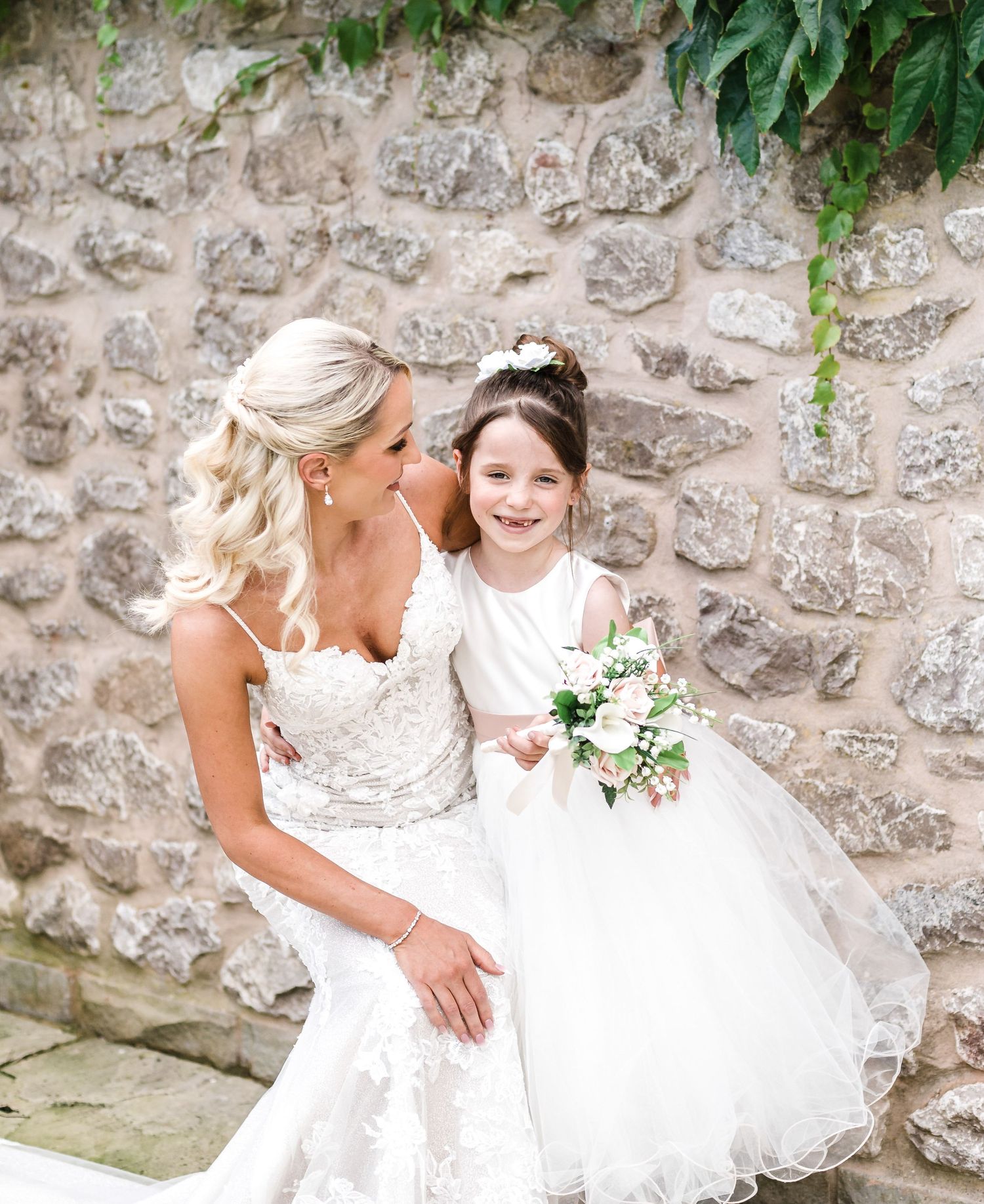 Sweet wedding moment captured against rustic stone wall with greenery.