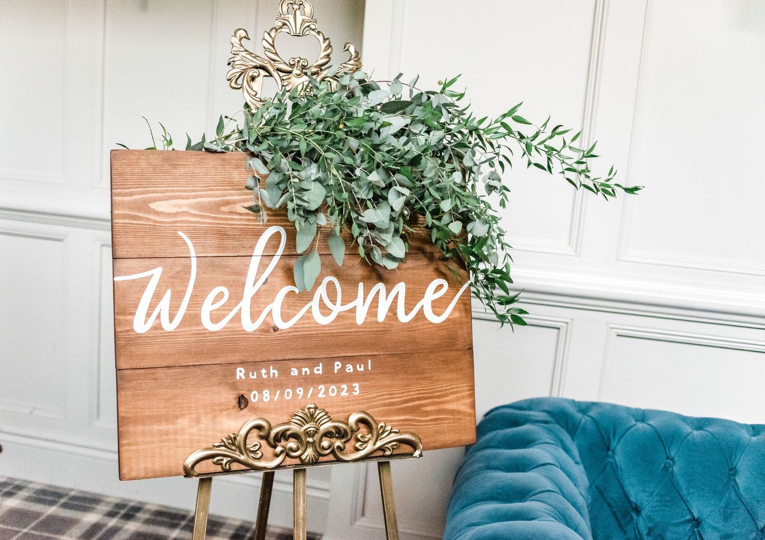 A rustic wooden welcome sign with white lettering and decorative gold accents.