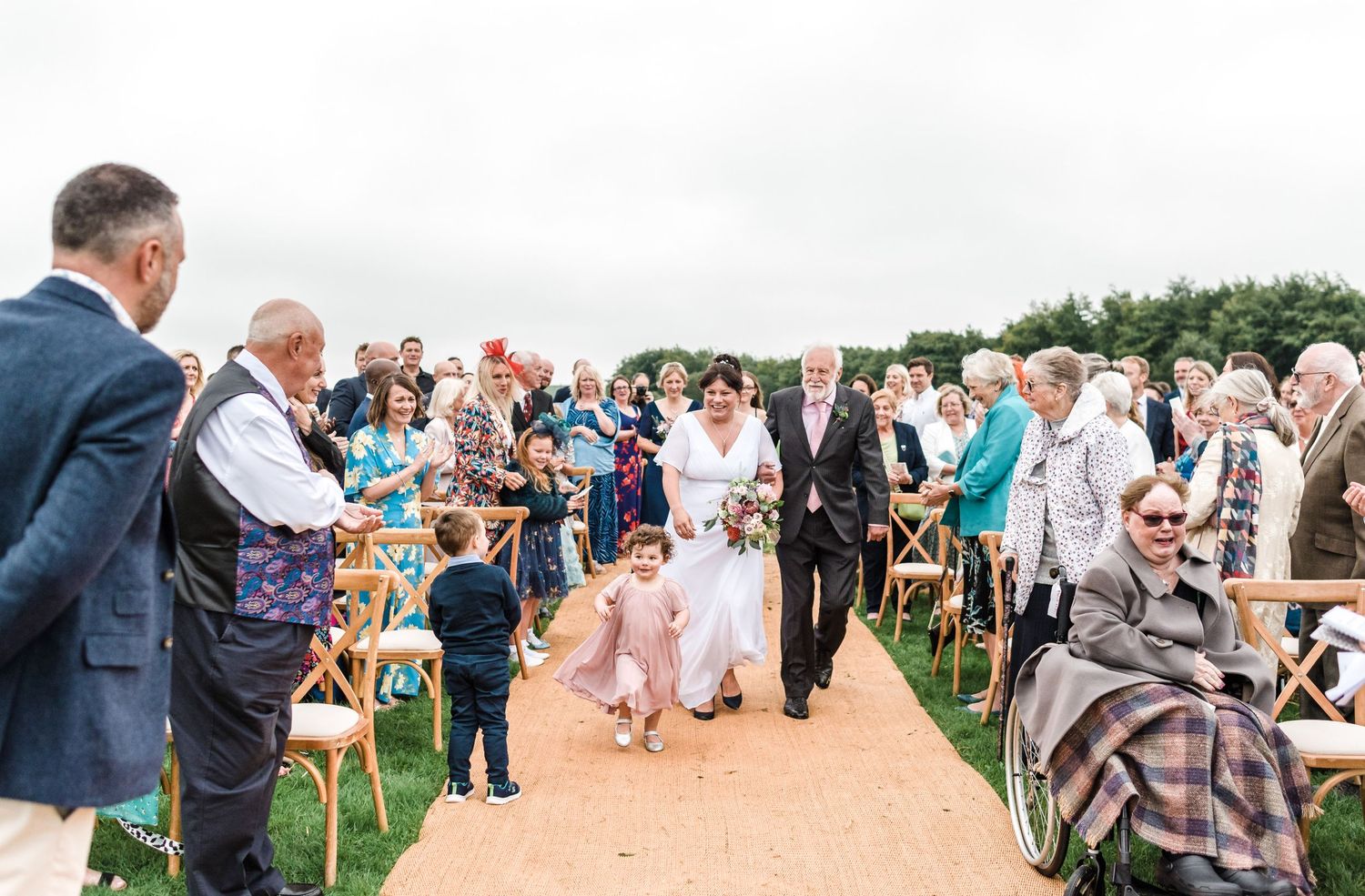 Wedding ceremony guests seated in wooden chairs along an outdoor aisle.