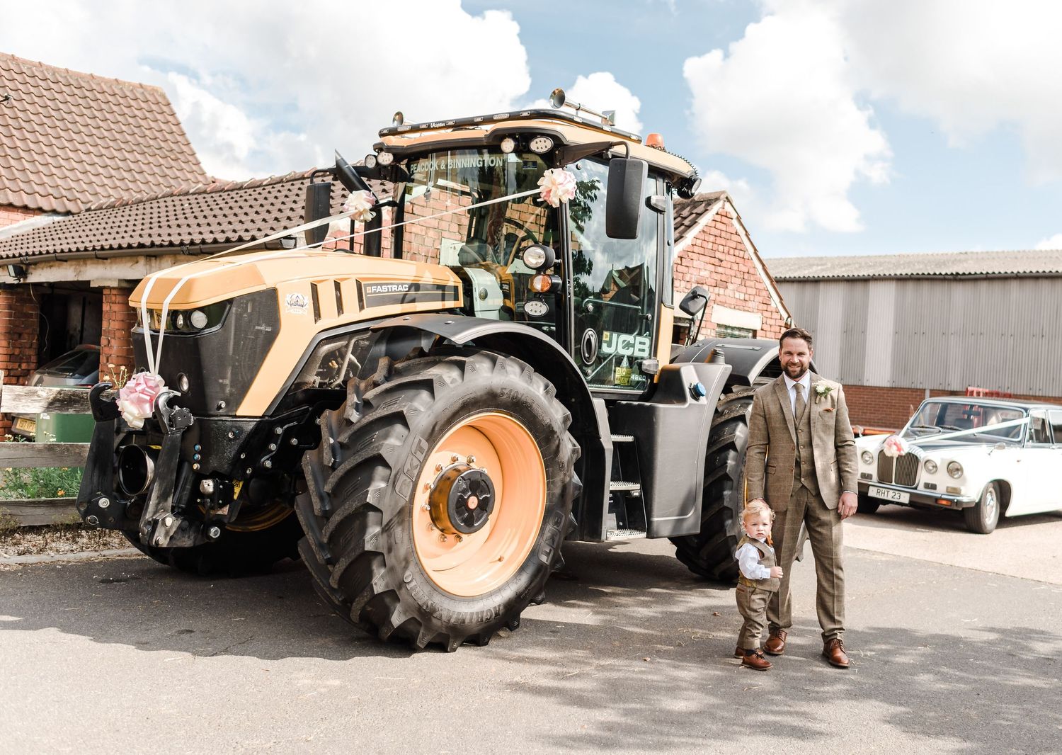 A large beige farm tractor parked outside brick buildings on a sunny day.