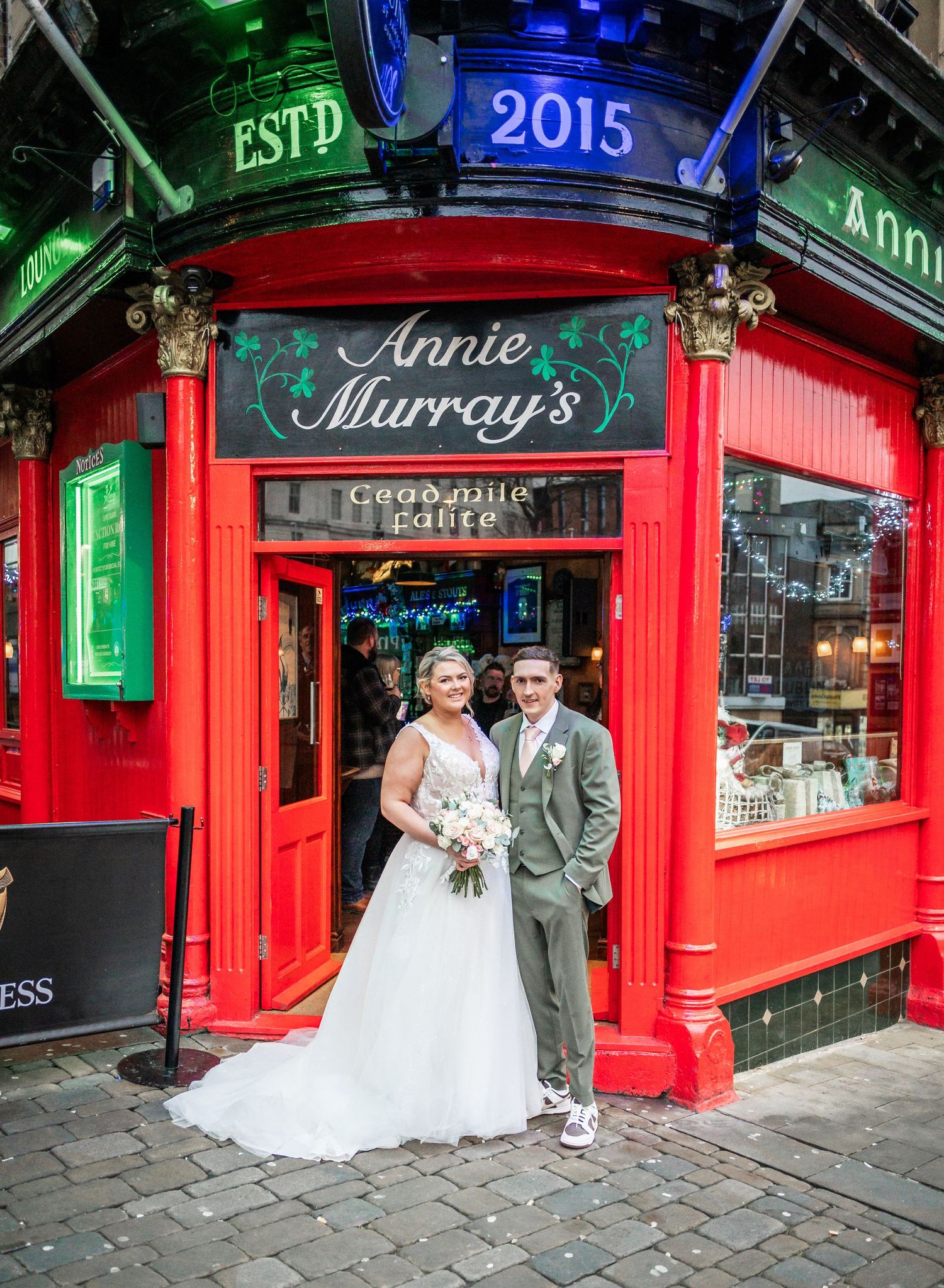 A wedding couple poses in front of the iconic red storefront of Annie Murray's pub in Edinburgh.