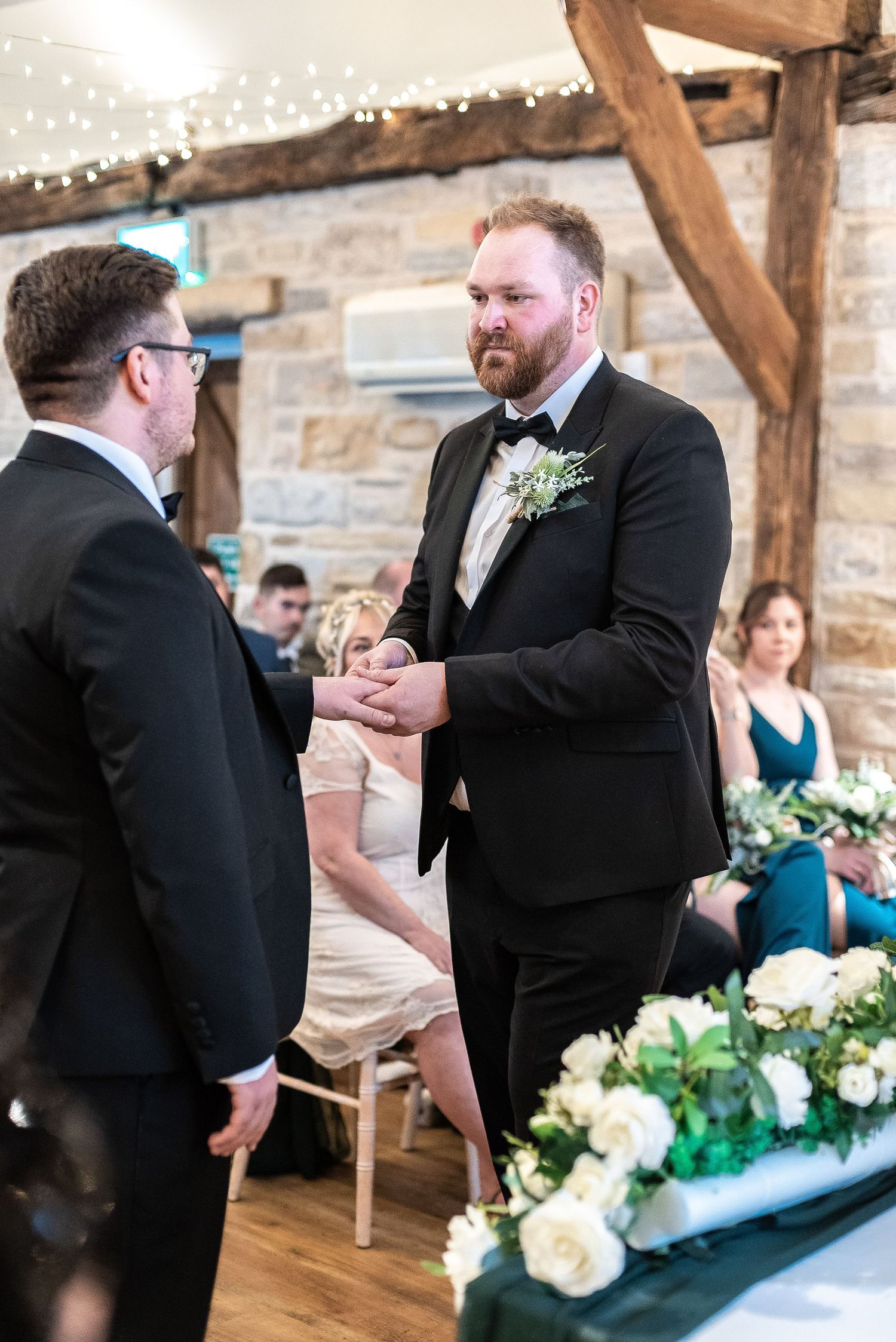 Wedding ceremony moment in rustic stone venue with wooden beams and floral decorations.