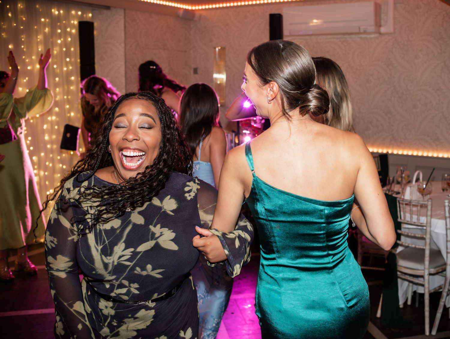 Wedding guests in formal attire dancing joyfully under ambient party lighting.