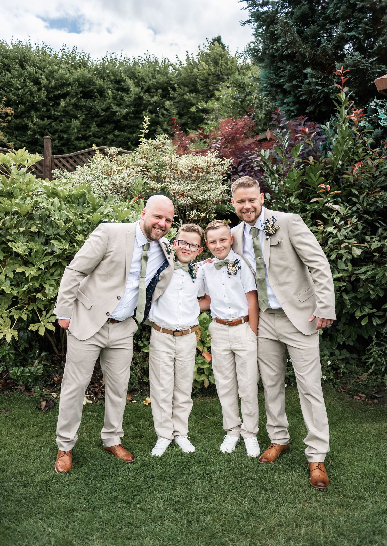 Wedding party in coordinated beige and white attire pose in a garden setting.