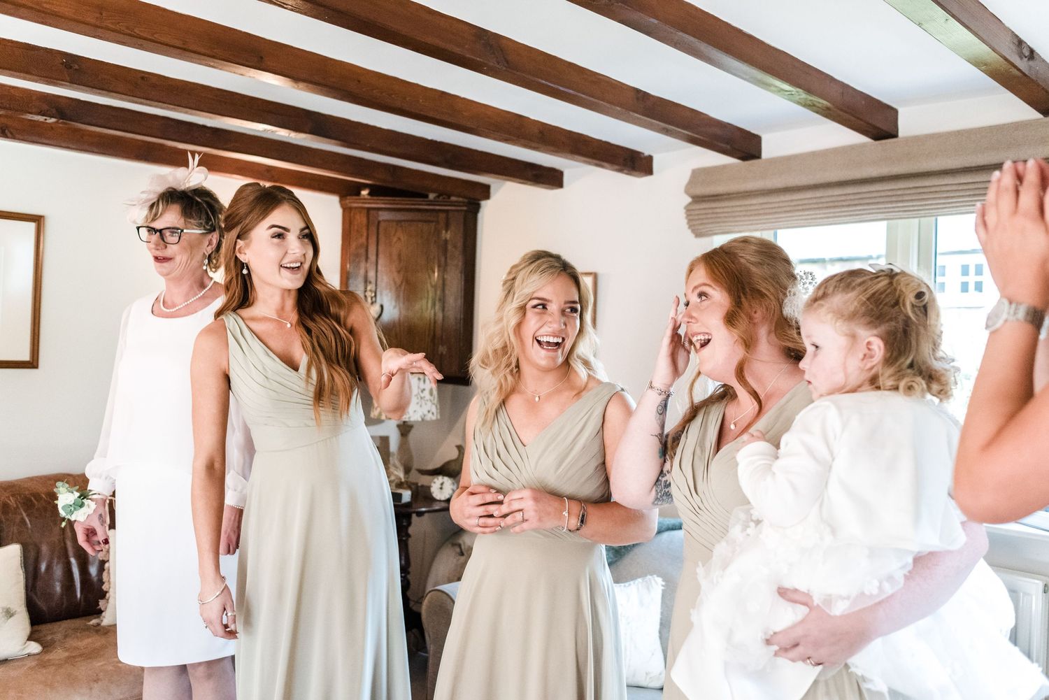 Candid moment of bridal party in neutral dresses sharing laughter during wedding preparations.
