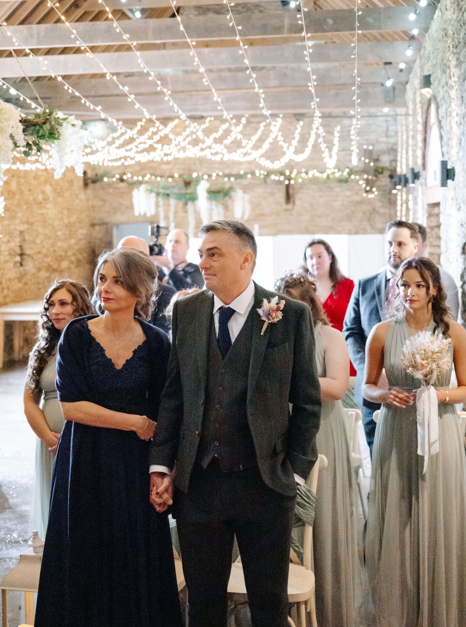 Wedding guests gather in a rustic venue decorated with twinkling string lights and exposed brick walls.
