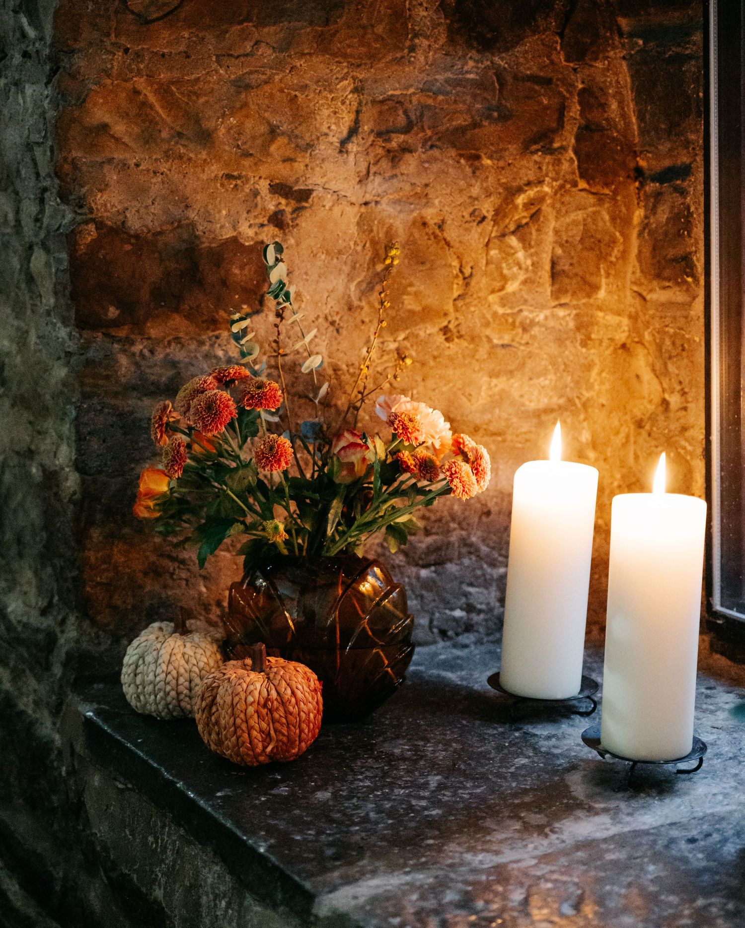 Rustic stone wall alcove decorated with glowing white candles and autumn pumpkin decorations.