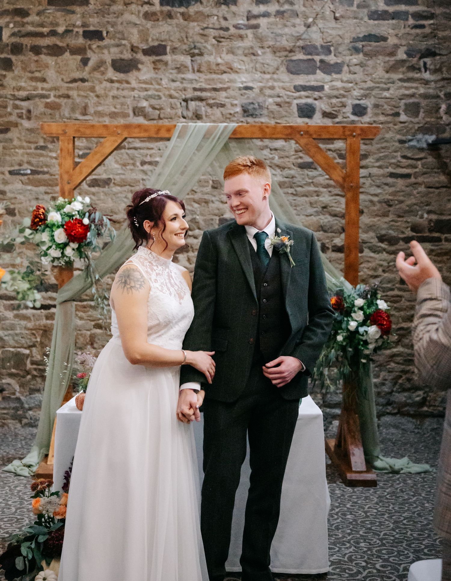 Wedding couple posing against rustic stone wall backdrop with wooden arch details.