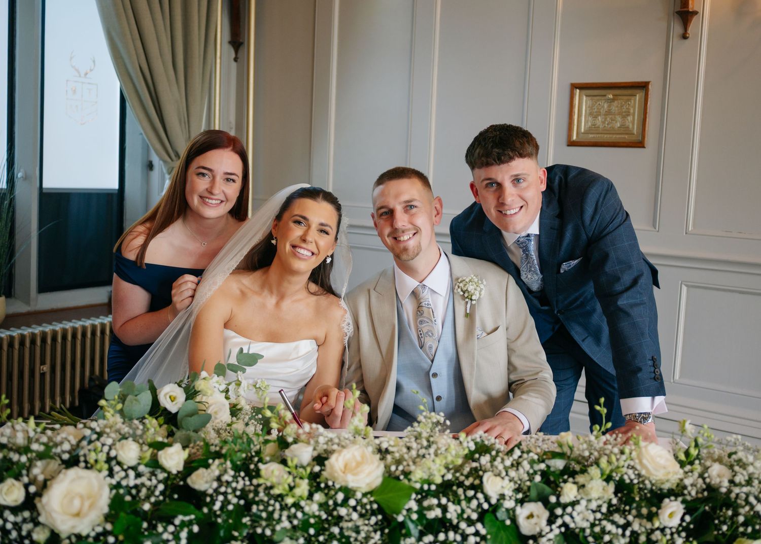 Wedding party gathered around floral-decorated table at reception.