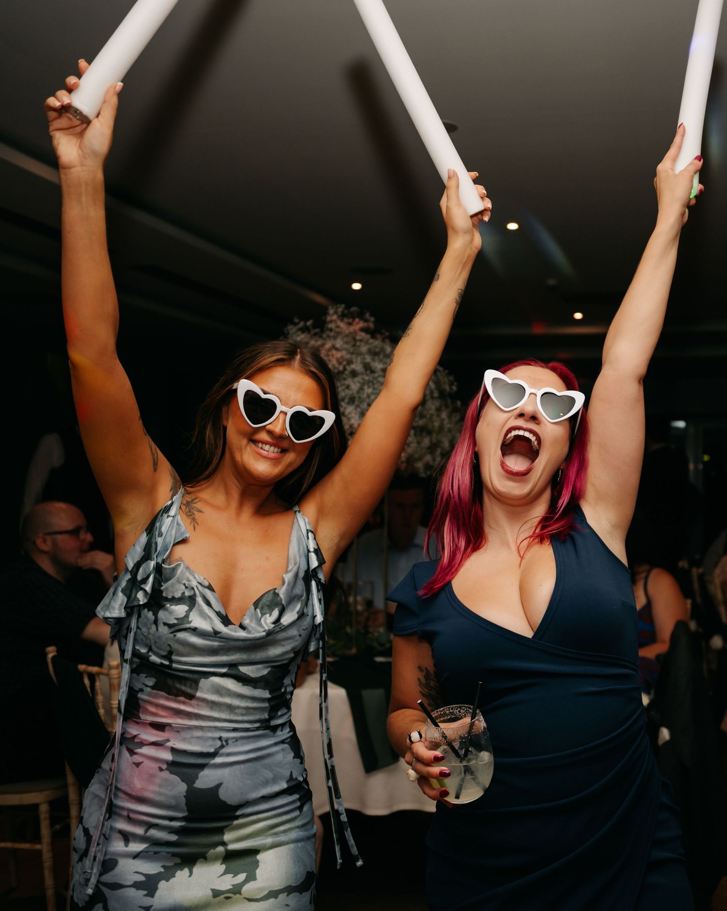 Wedding guests dancing with glow sticks and sunglasses at night reception.