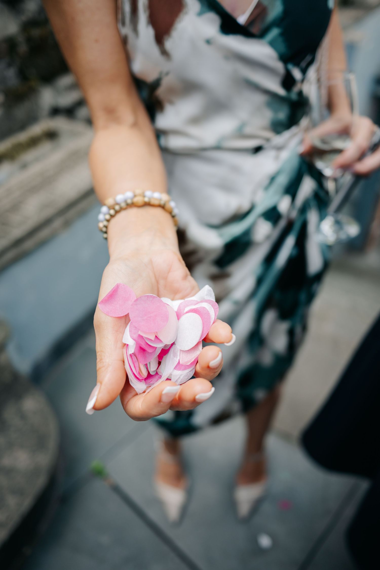Hands holding delicate pink flower petals at an outdoor wedding ceremony.