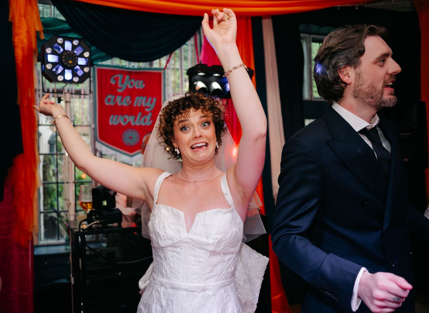 Couple celebrates joyfully under red lighting at their wedding reception.