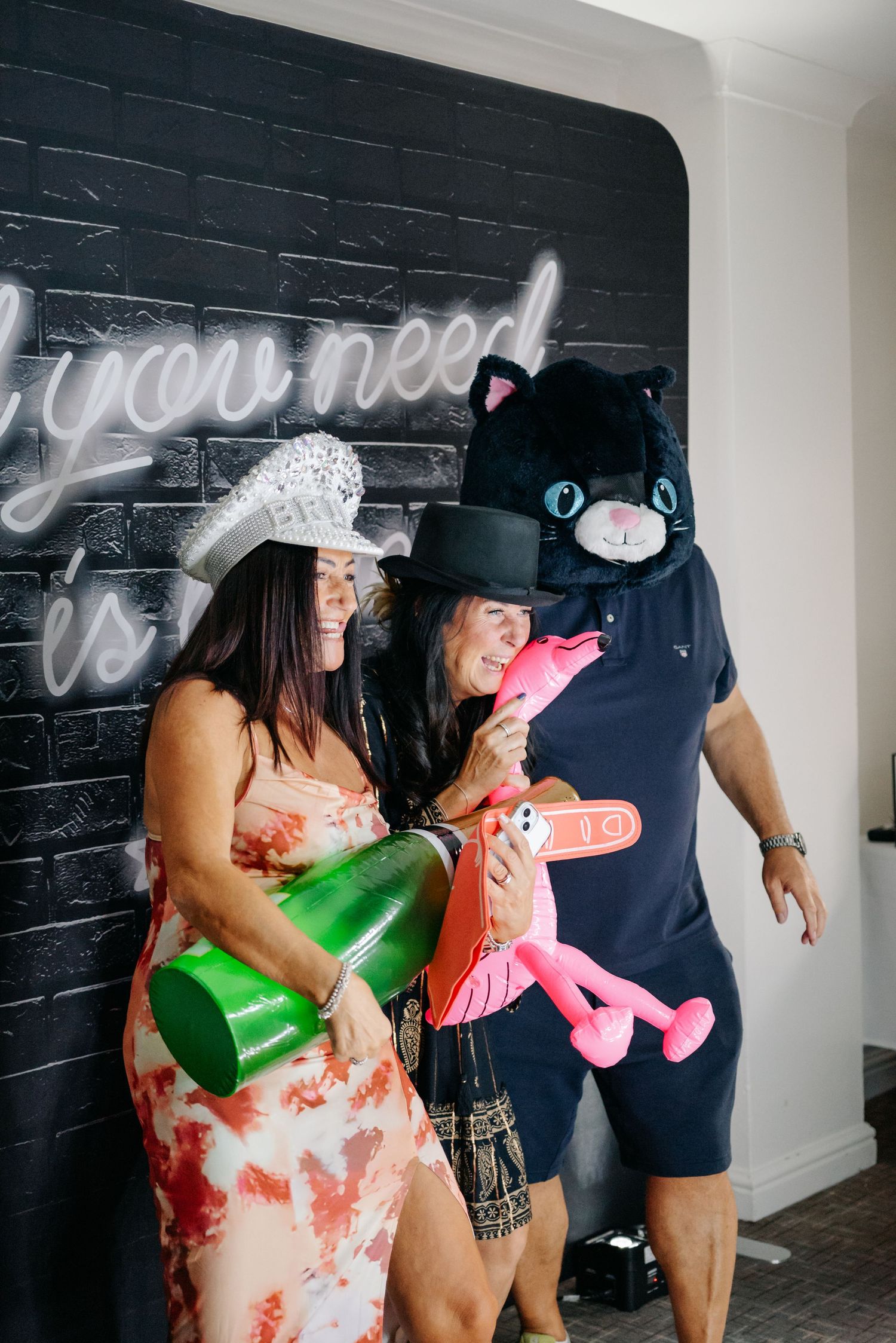 Party guests in costumes and hats pose playfully against a black wall with neon signage.