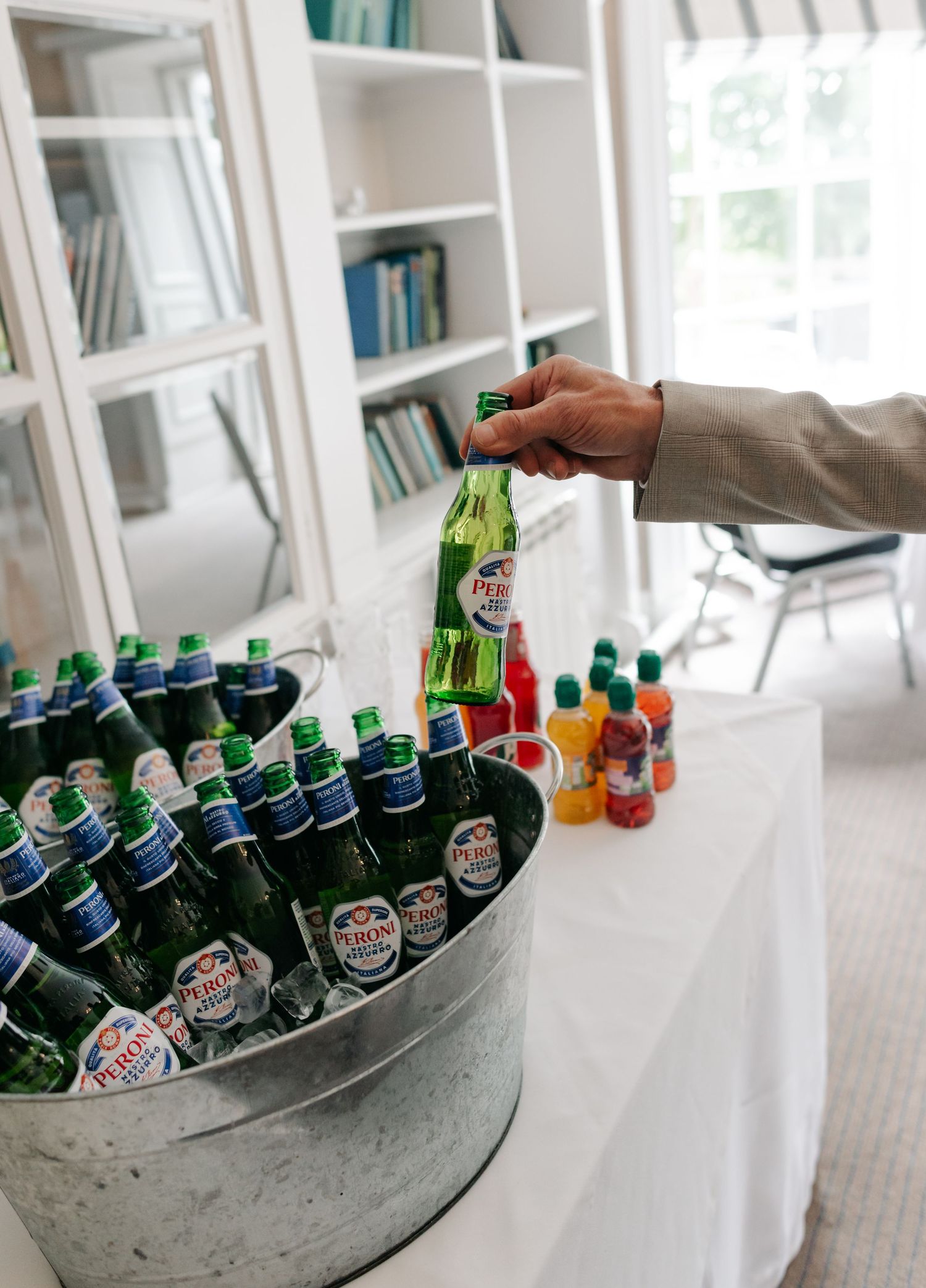 Assorted glass bottles of beverages chilling in a galvanized metal tub filled with ice.