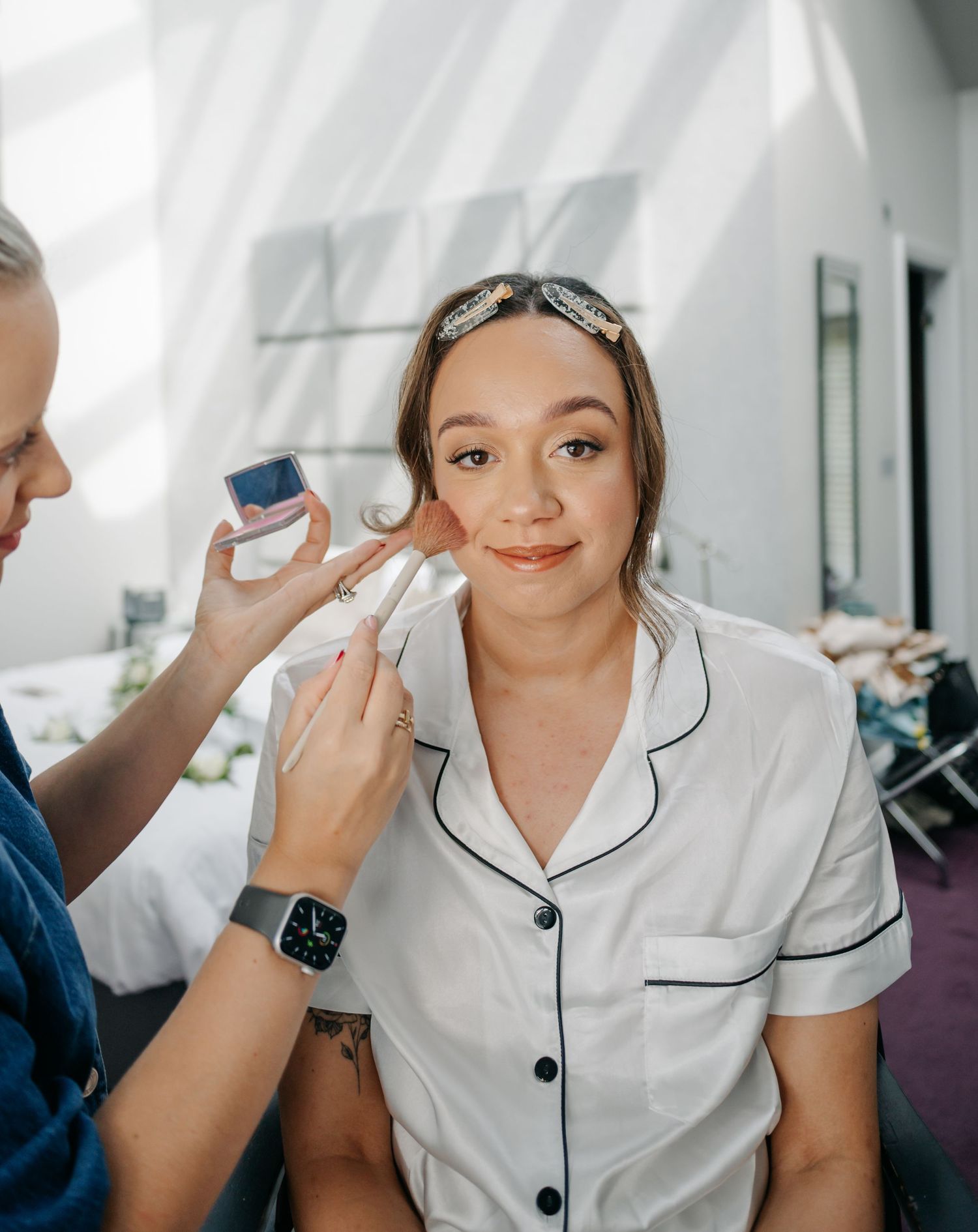 Person in white pajamas getting makeup applied during wedding preparation.