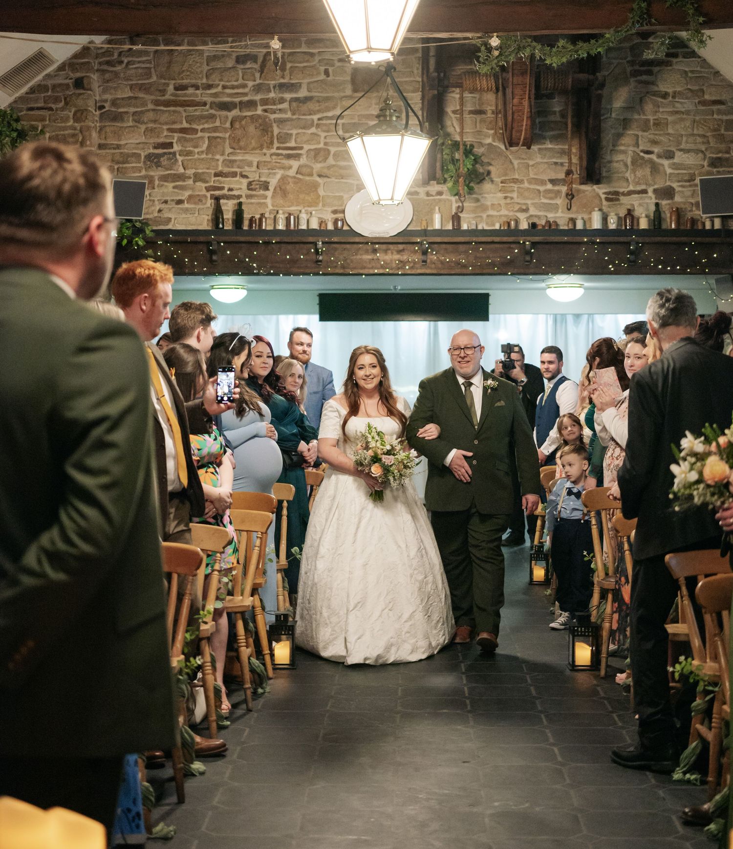 Wedding ceremony in a rustic stone venue with wooden chairs and string lights.