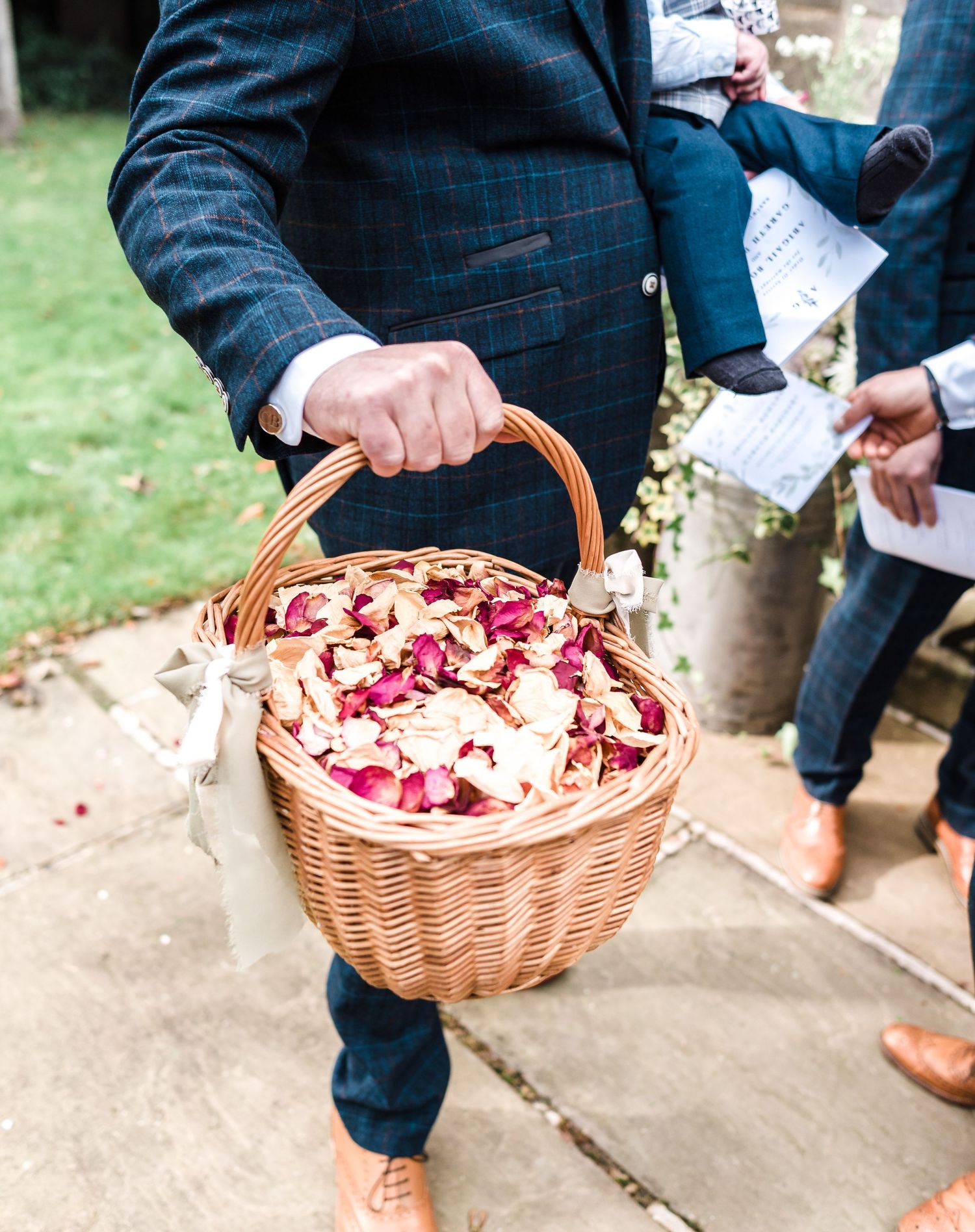 A wicker basket filled with pink and white flower petals is held at a wedding ceremony.