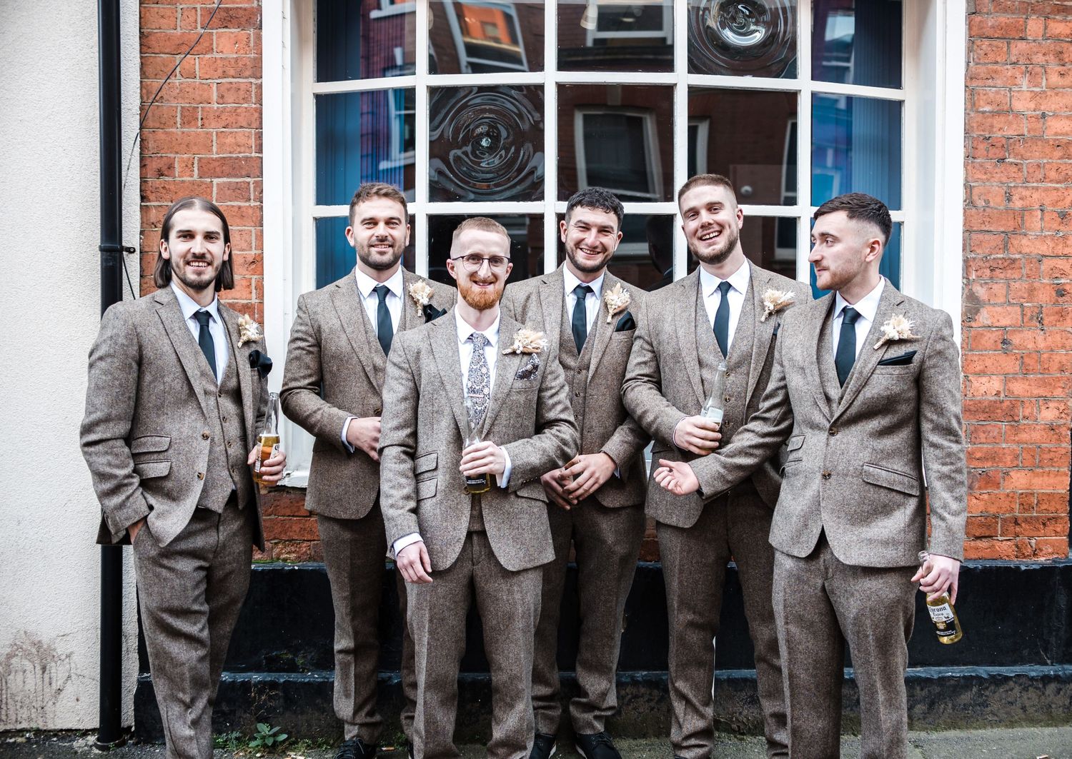 Groomsmen in matching grey suits pose together outside a historic building entrance.