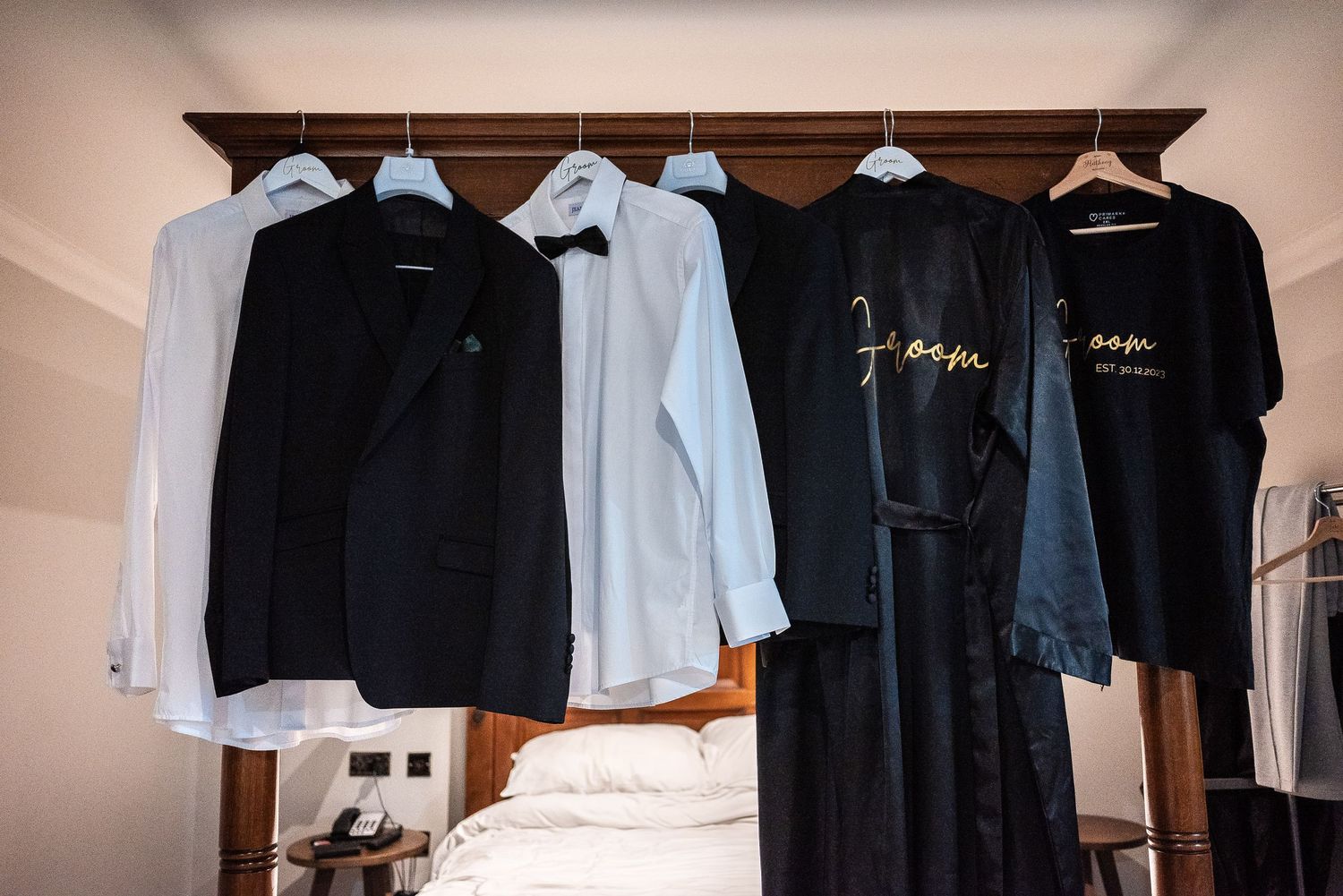 Wedding attire including black and white formal wear hanging on wooden hangers.