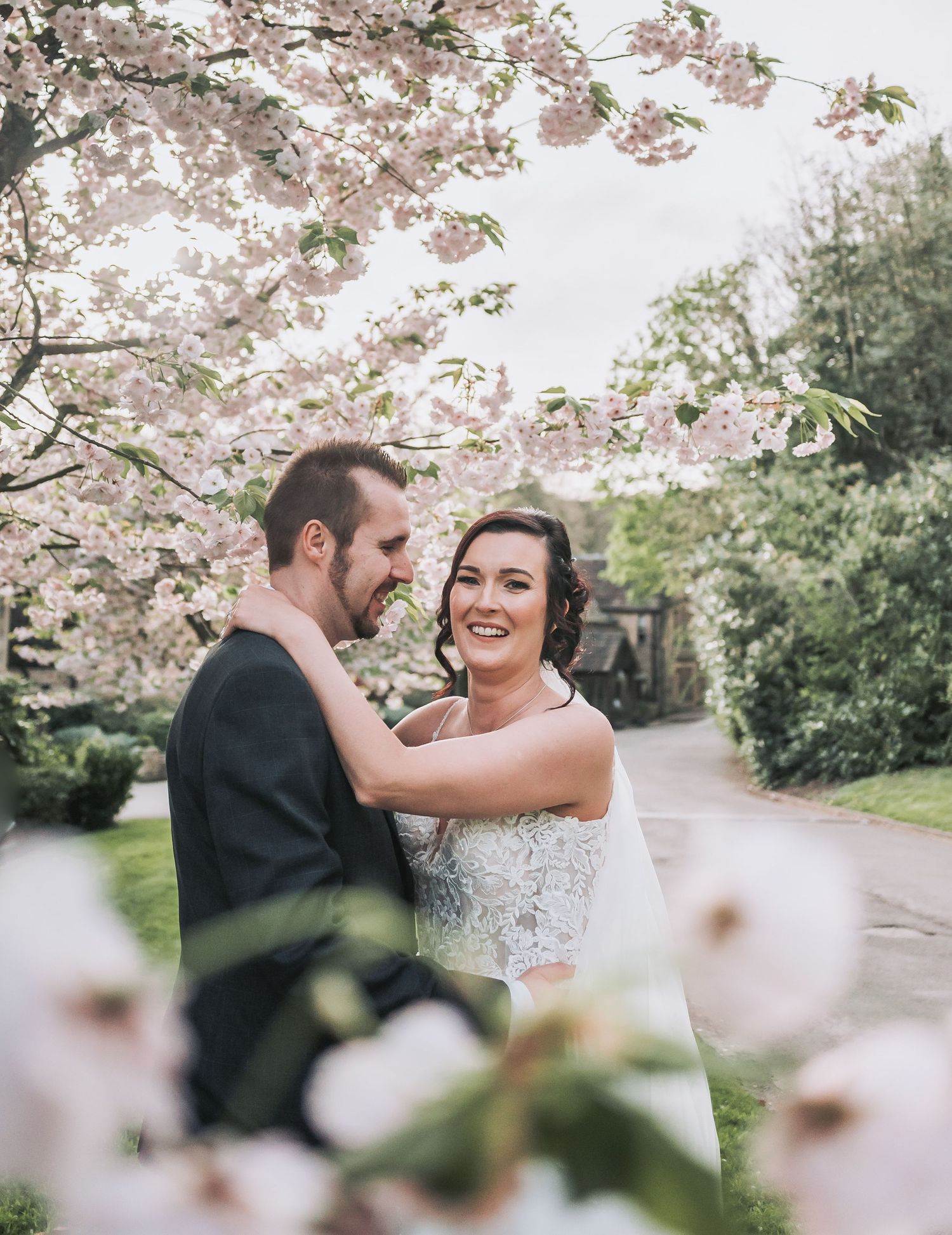 Romantic wedding portrait beneath pink cherry blossoms with laughter and joy.