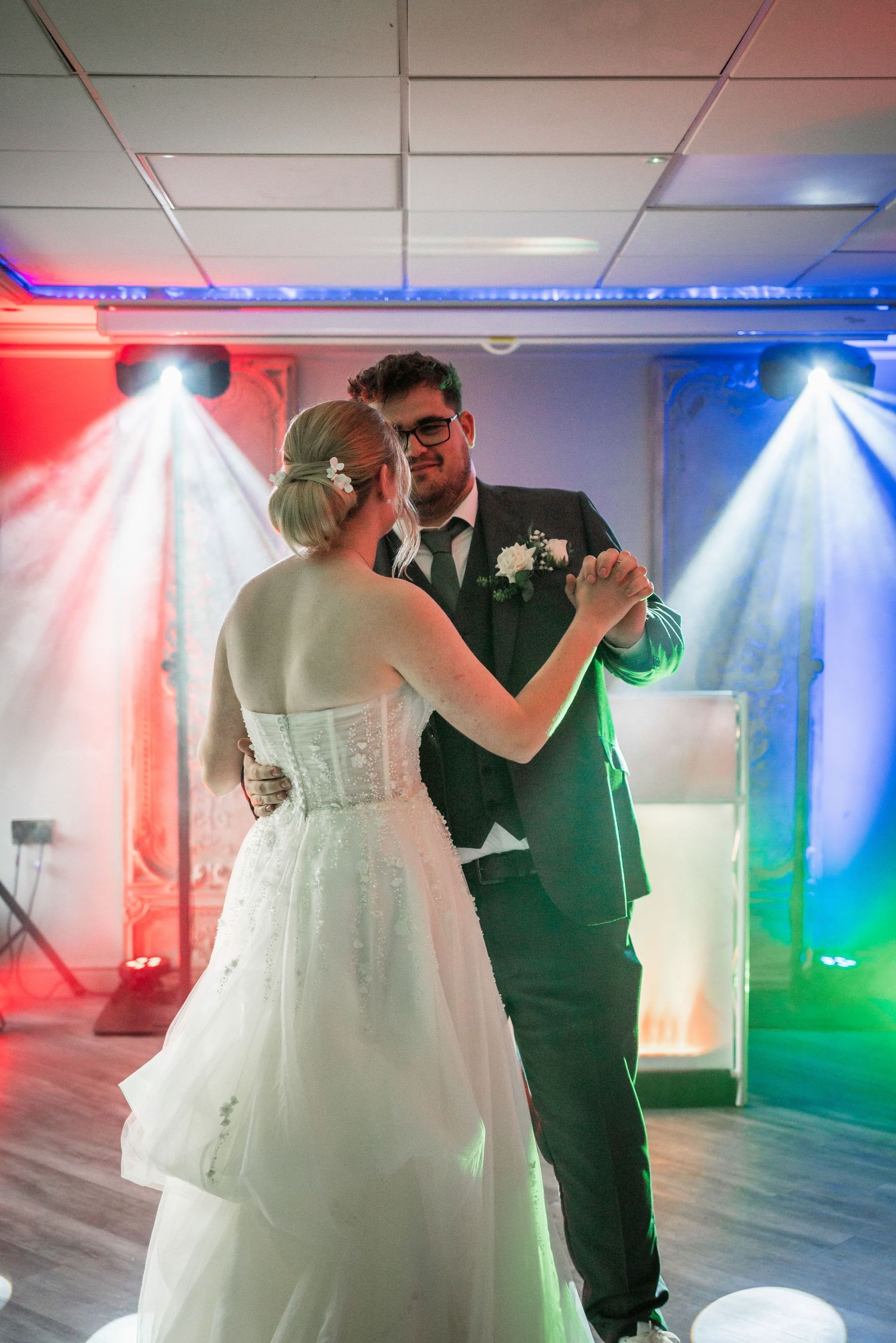 Wedding couple shares first dance under colorful red and blue spotlights.