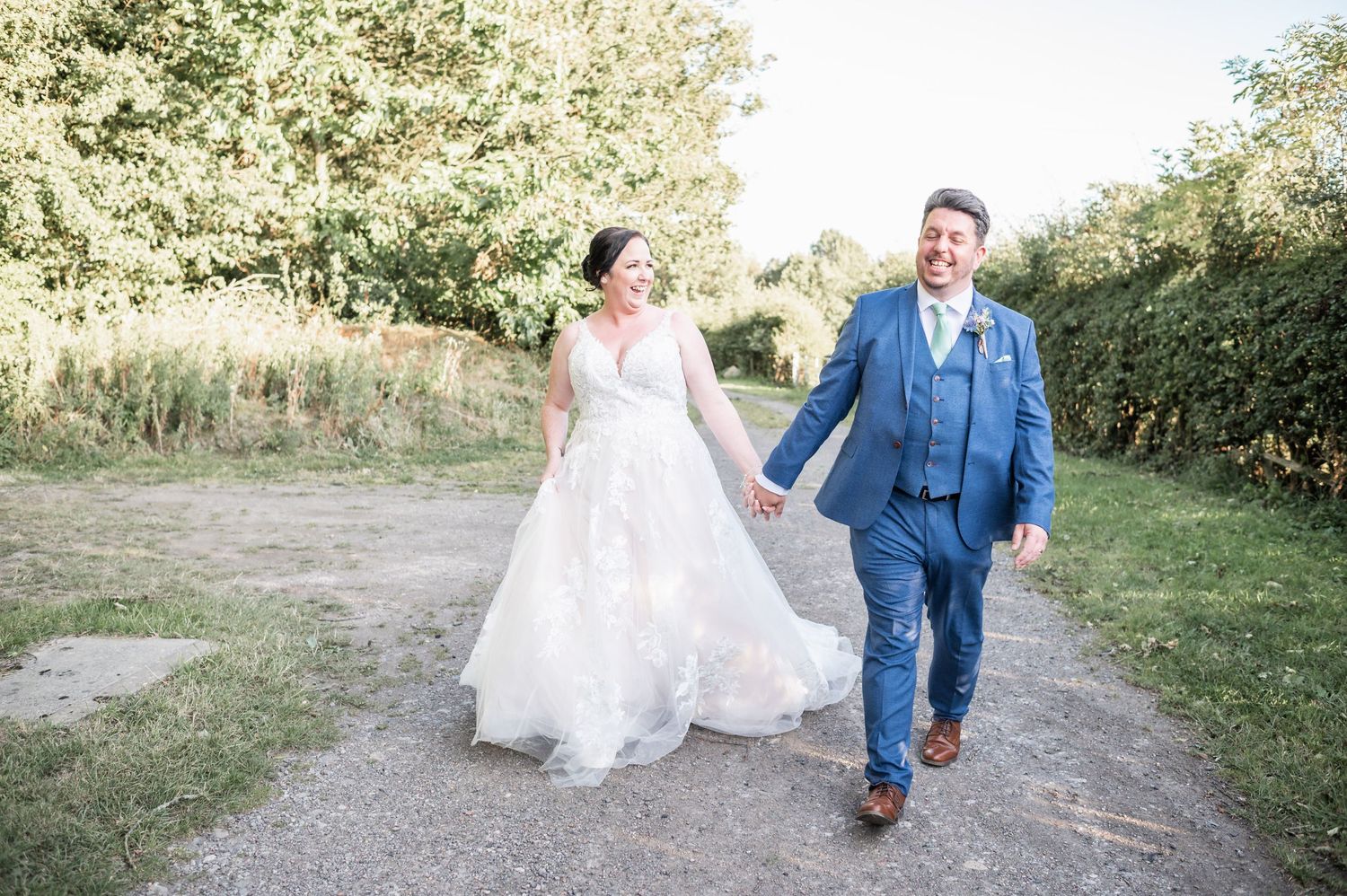 Joyful couple walking together on outdoor path during wedding celebration.