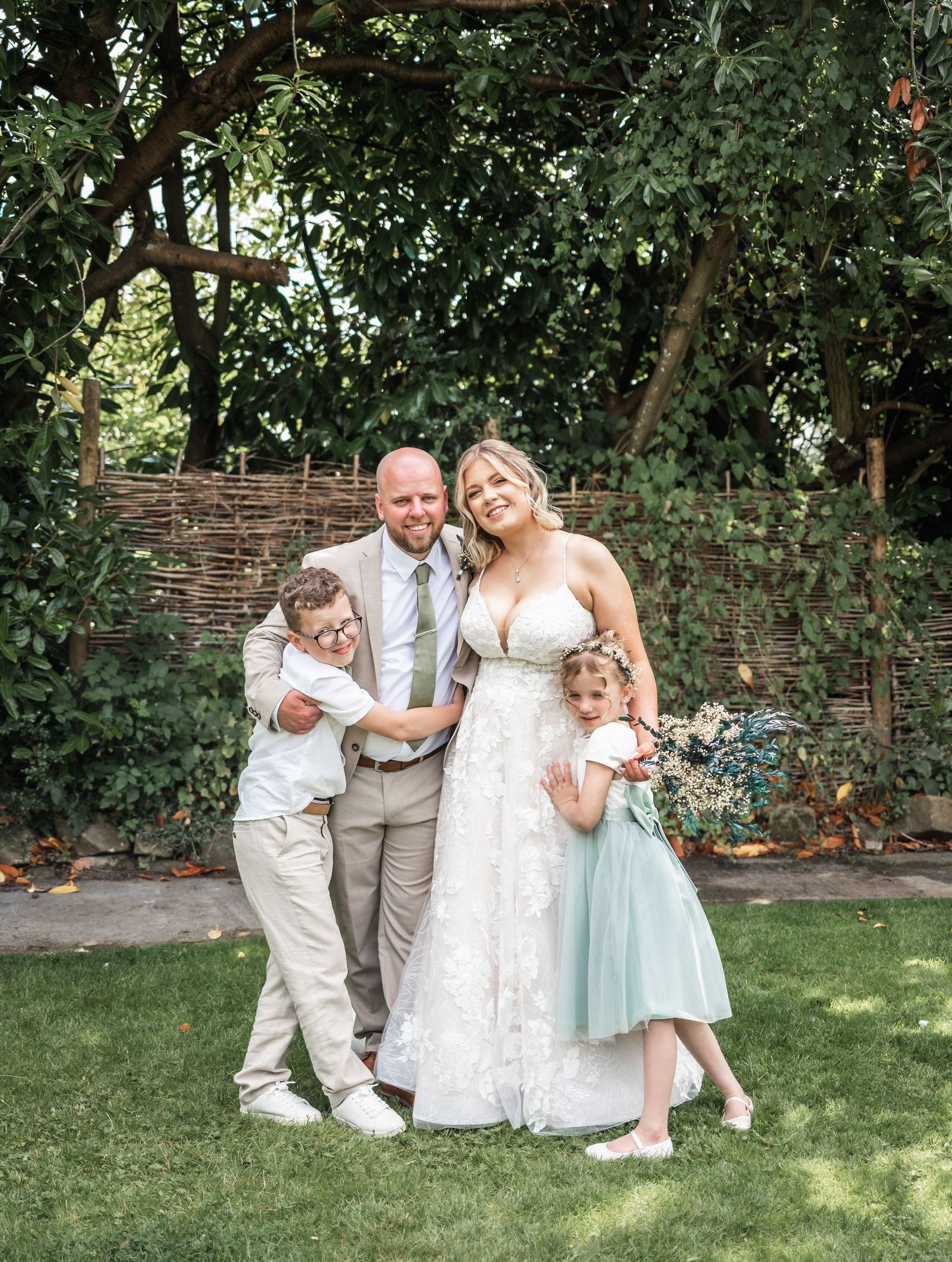 Wedding portrait in garden setting with bride in white dress and children in formal attire.