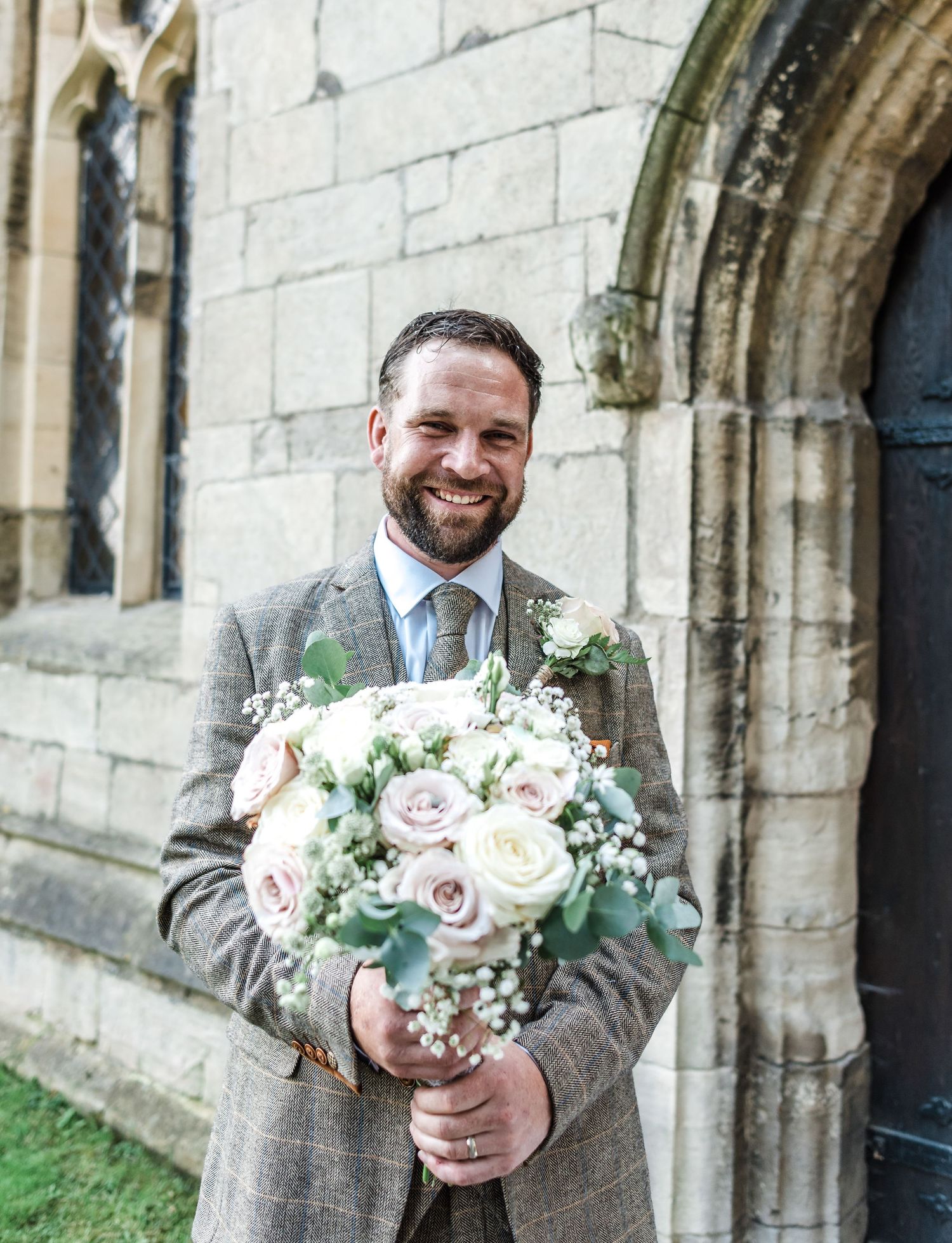 Groom in grey suit holding elegant white and pink rose wedding bouquet.