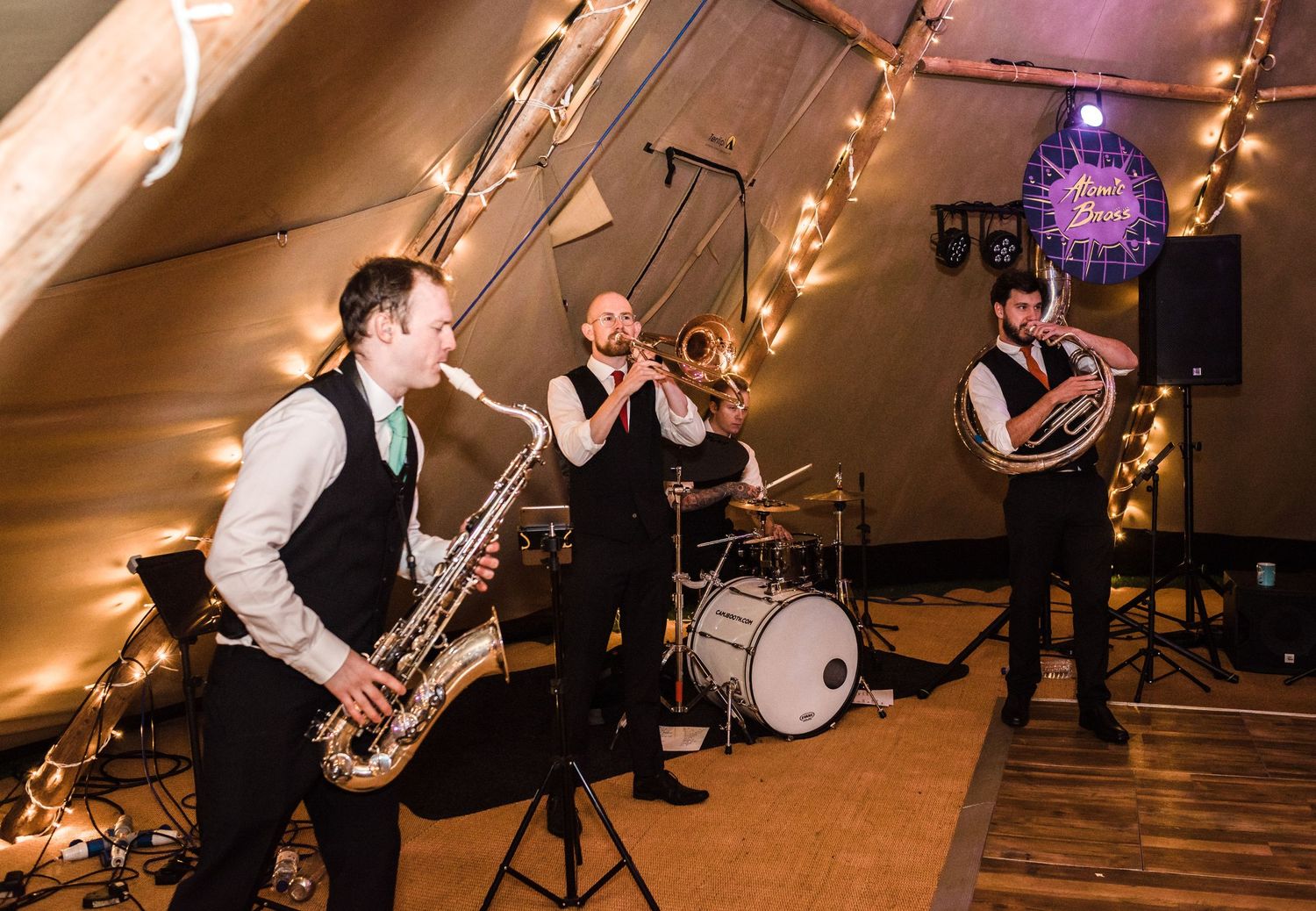 Wedding band musicians performing with saxophone and instruments in a decorated tent venue.