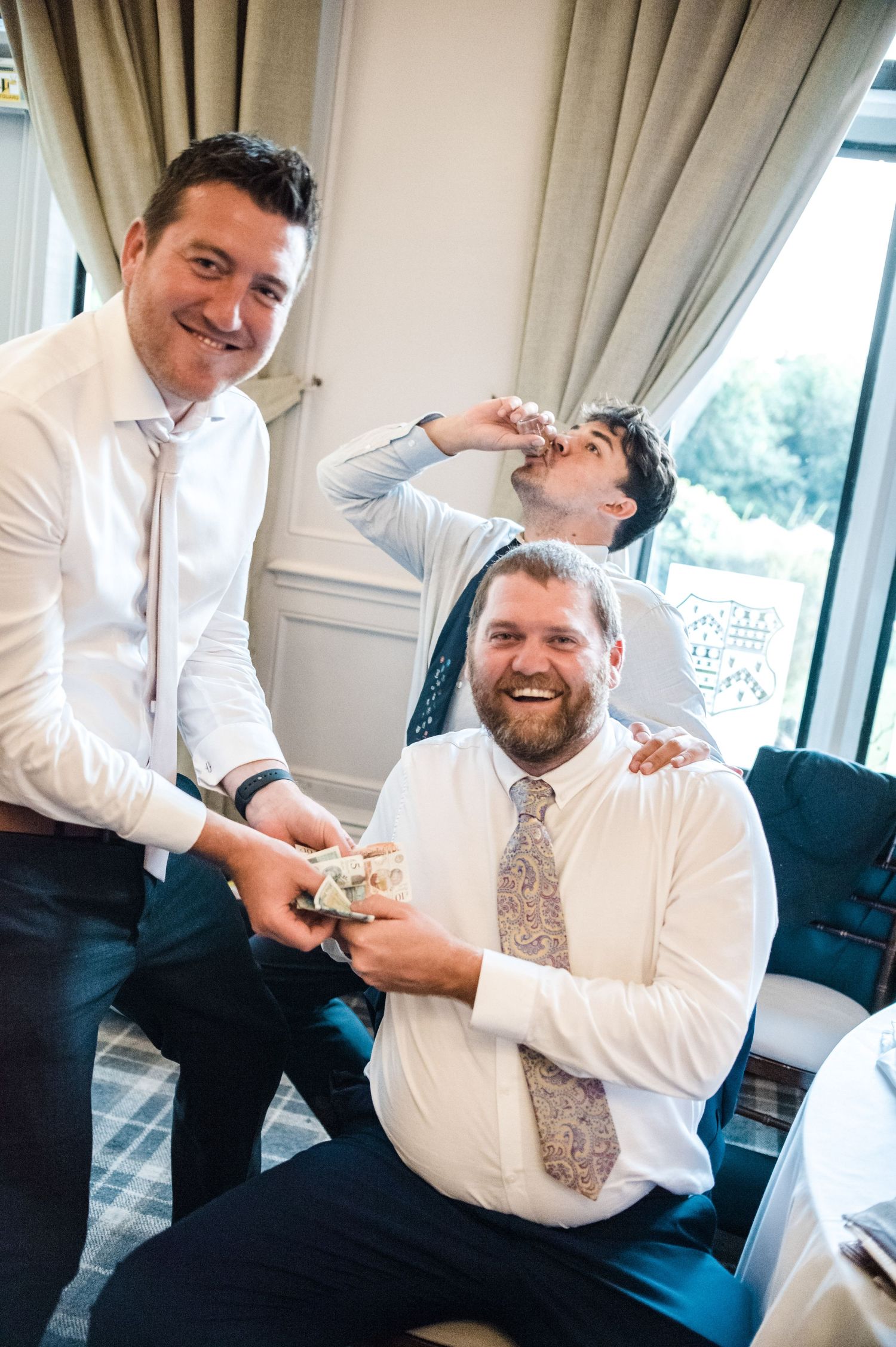Three guests sharing playful moment during wedding reception in elegant venue.