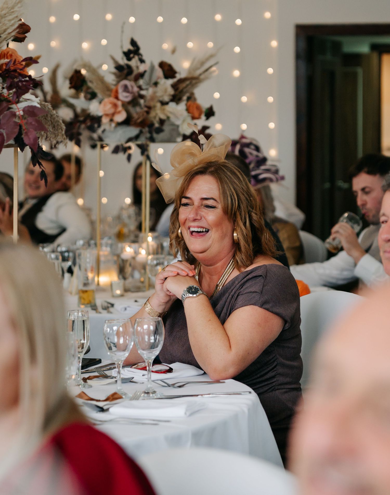 Wedding reception guests sharing laughter at decorated dining tables with string lights overhead.