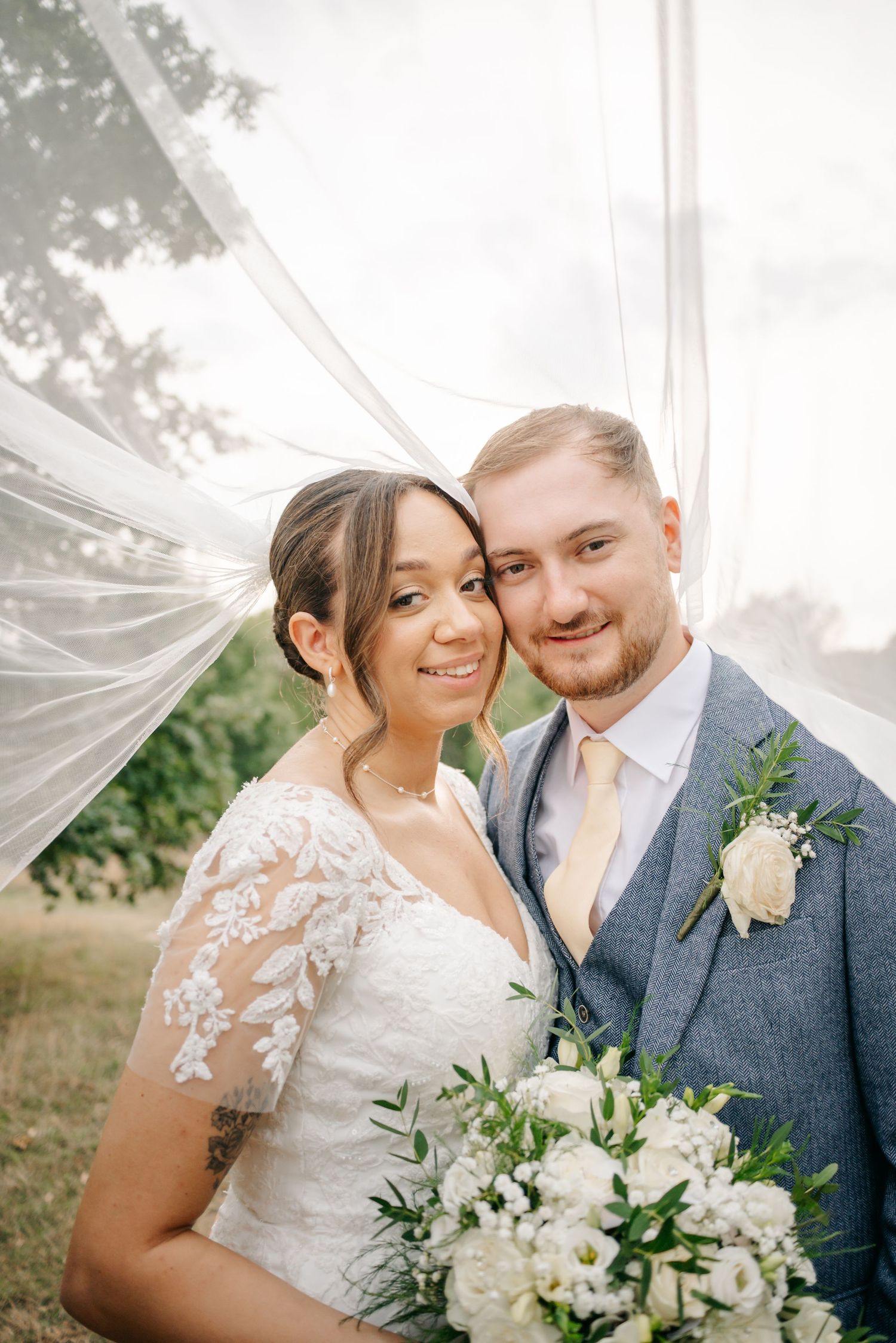 A couple shares an intimate moment under a flowing veil in an outdoor setting.